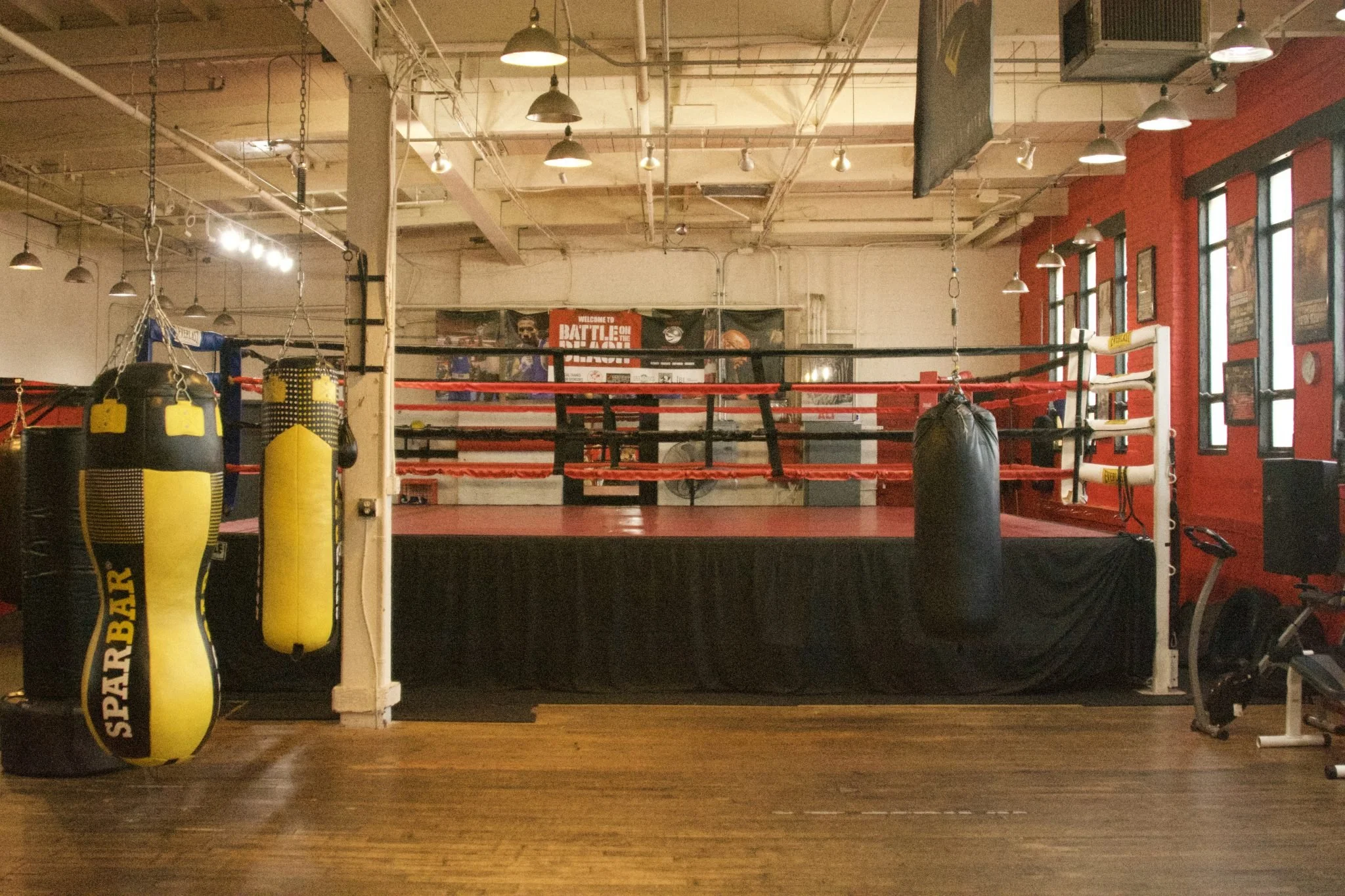 Professional boxing gym interior with red and black boxing ring, heavy bags, and industrial lighting