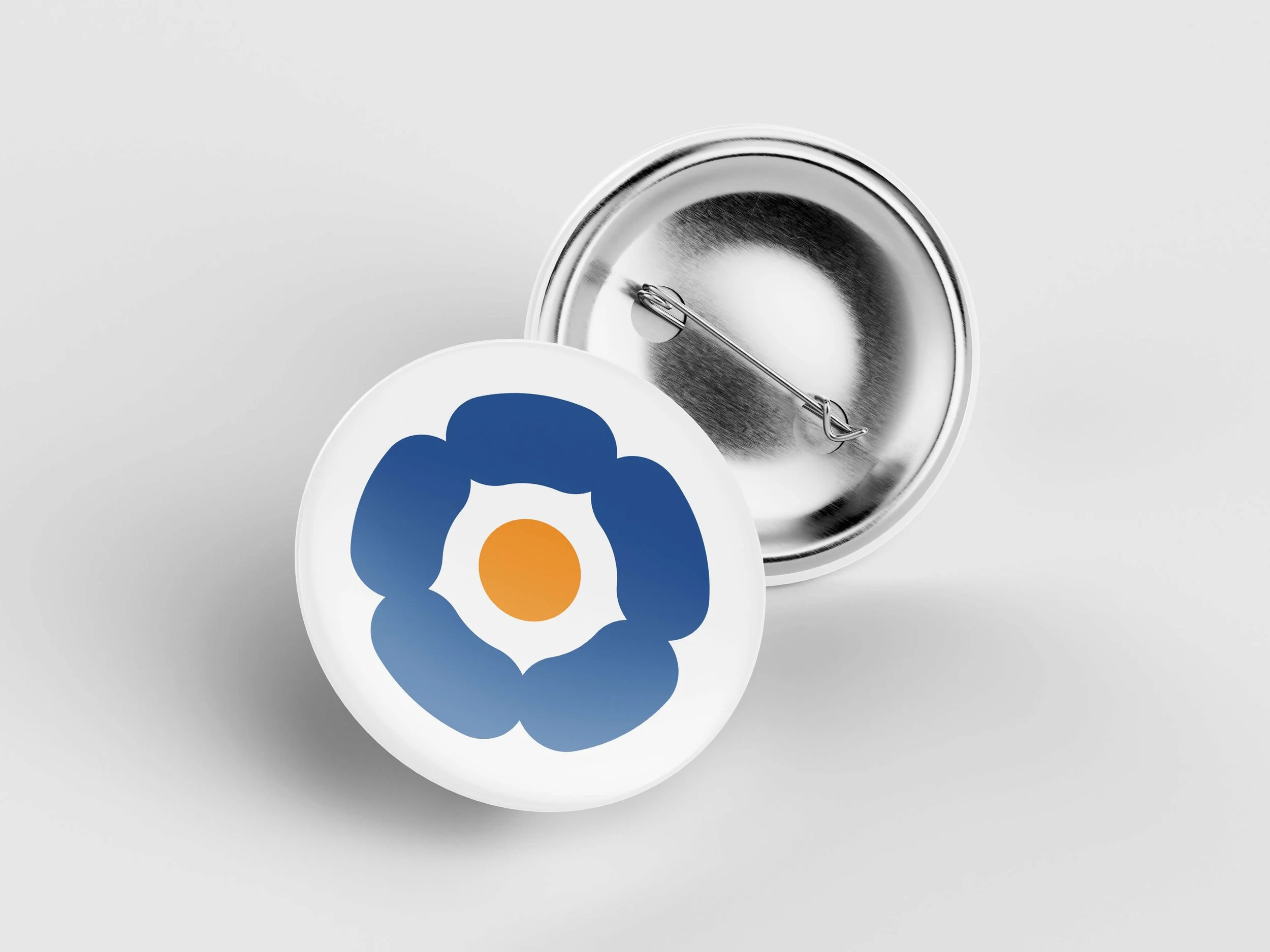 A round pinback button featuring a stylized blue flower with a yellow center, shown from the front, with the back of the button up, revealing the pin mechanism.
