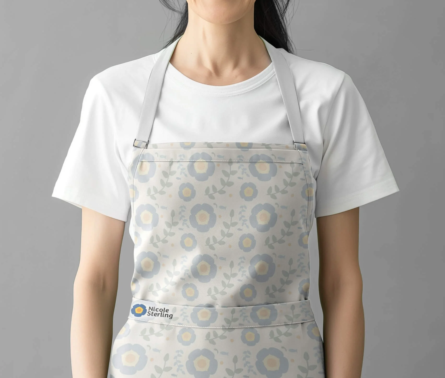Person wearing a white T-shirt and a floral apron with a name tag that says "Nicole Sterling".