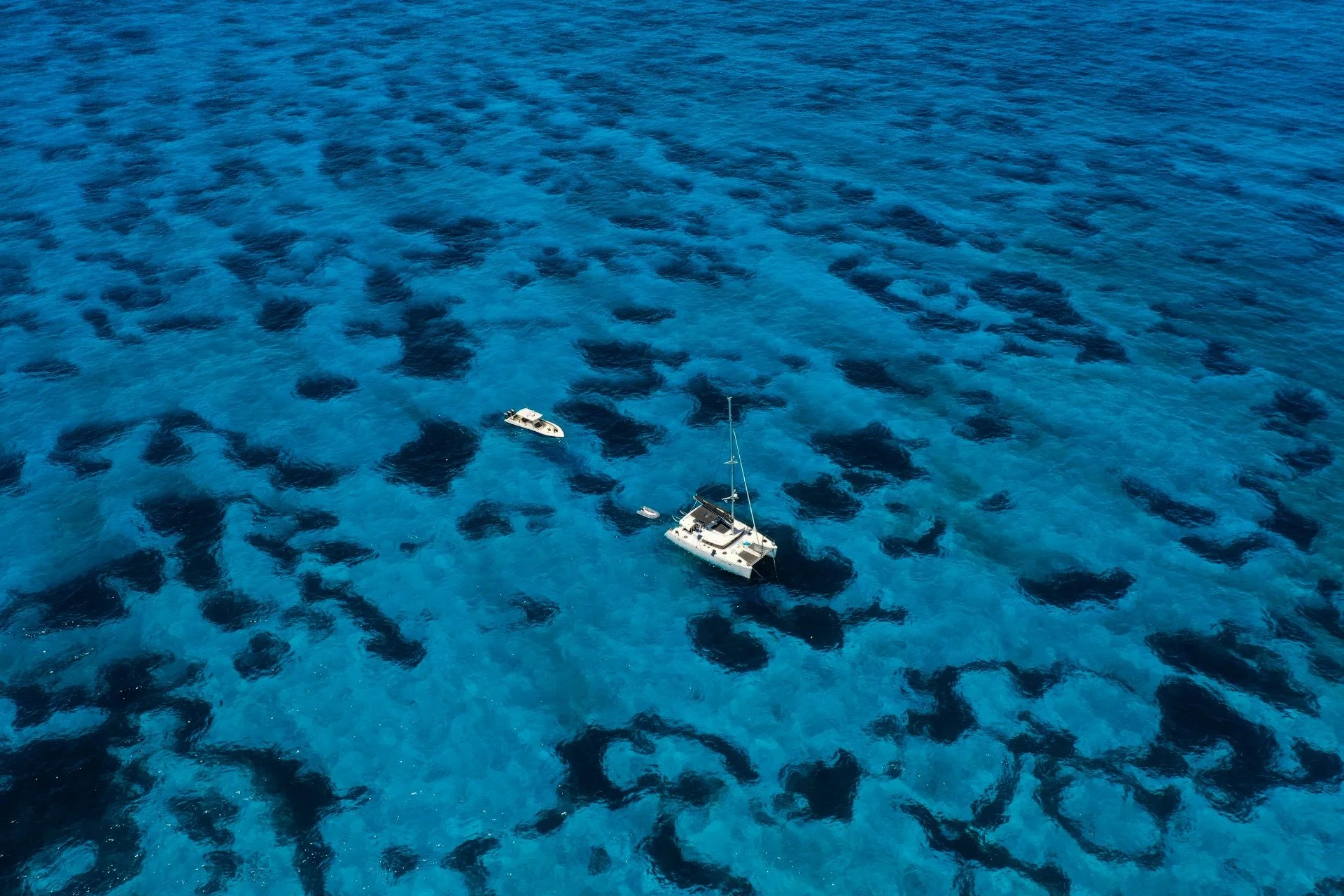 Aerial view of two boats floating on clear blue ocean water with coral reef patches visible beneath the surface
