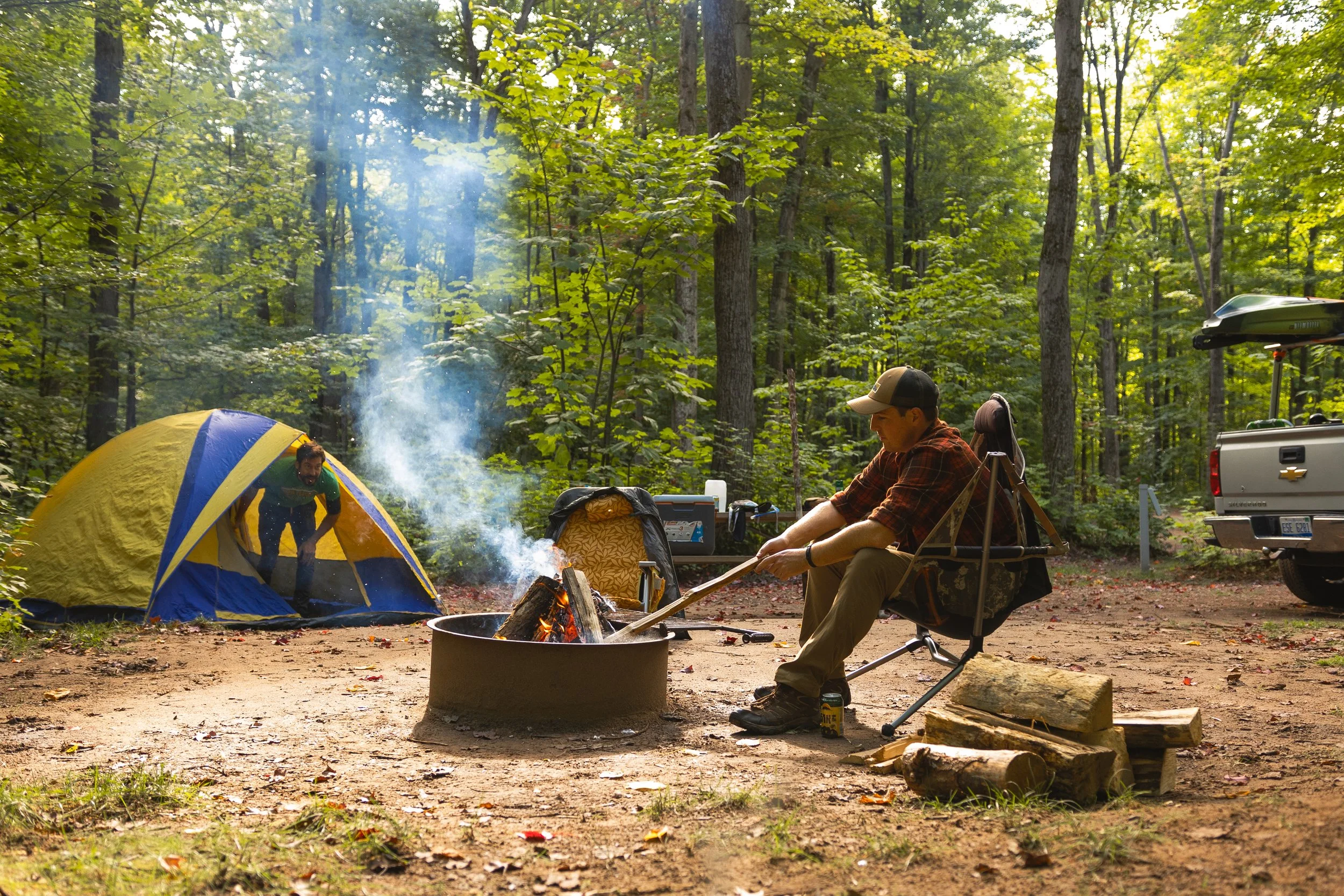 Man stoking a bonfire with a tent in the background camping in Marquette Michigan