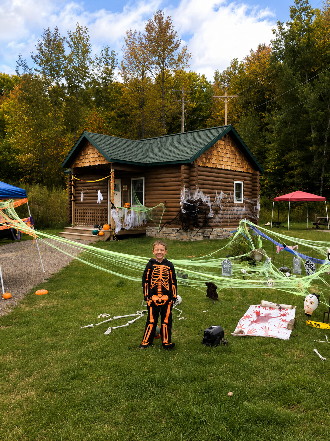 Child in a skeleton Halloween costume standing in front of a decorated cabin during Harvest Fest Weekend.