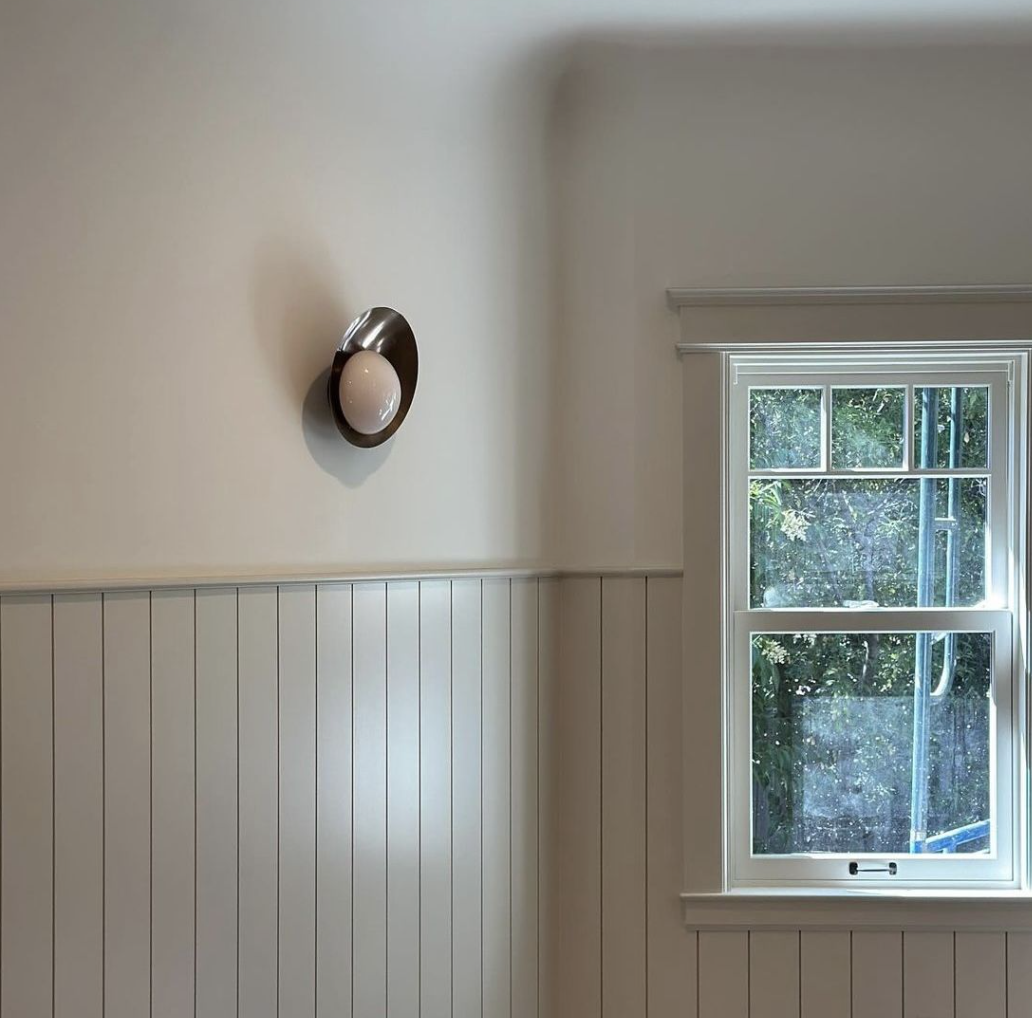 Interior view of a room with a wall-mounted light fixture and a window showing outdoor greenery.