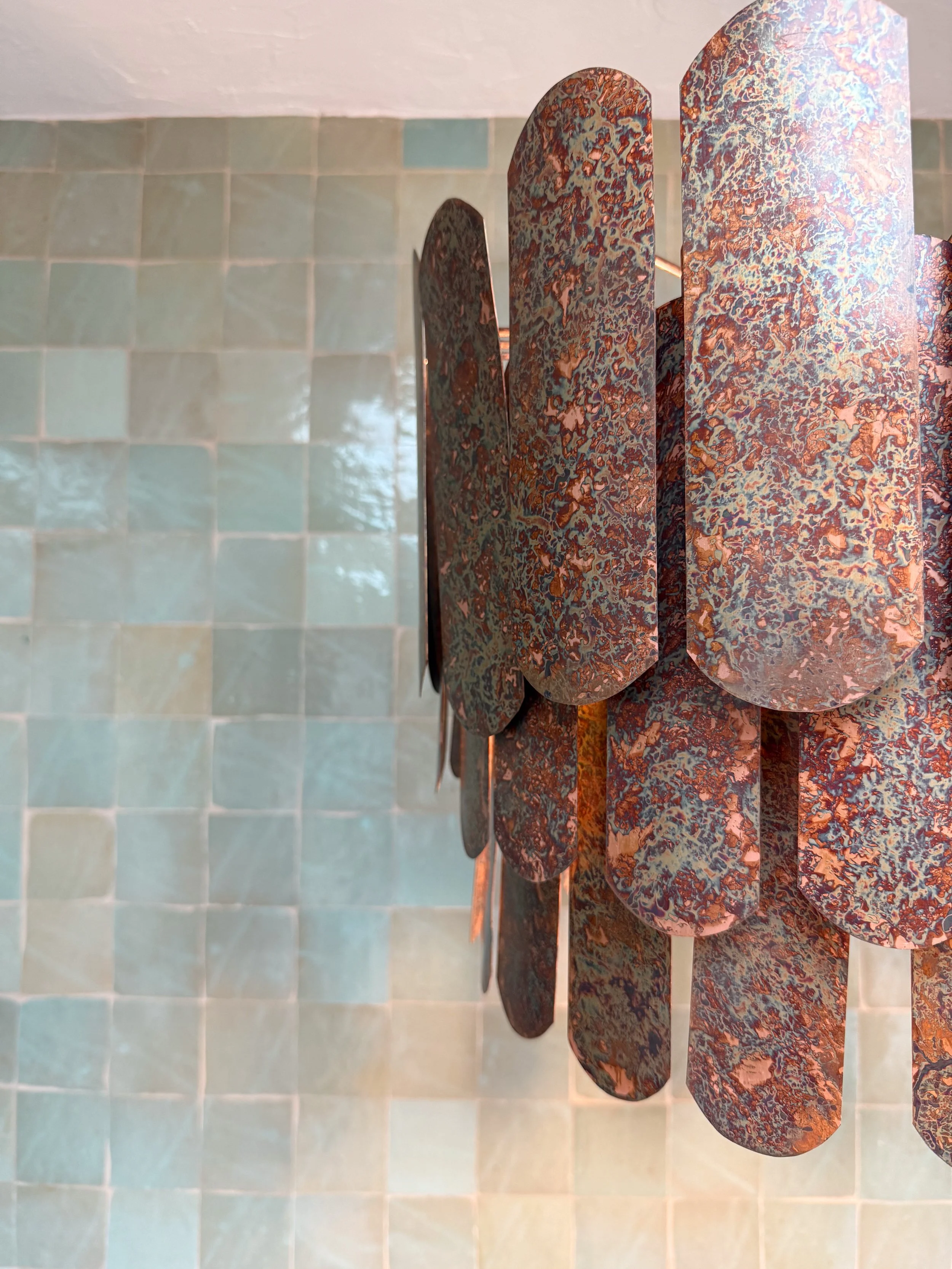 Close-up of a rusted metal sculpture with layered, oval-shaped pieces against a tiled wall.