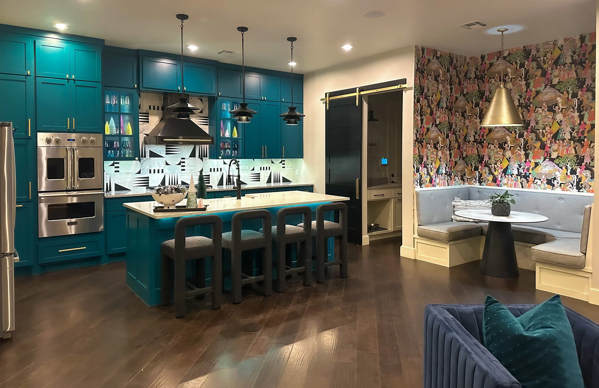 Modern kitchen with teal cabinetry, white marble island, black pendant lights, geometric backsplash, and a newspaper print nook with a round table and gray corner bench seating.