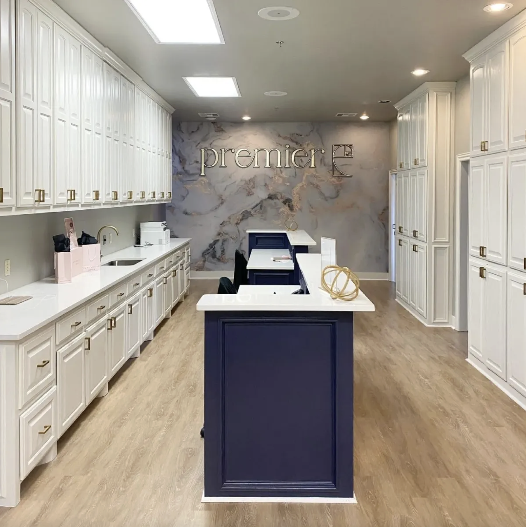 Interior of a modern office or reception area with white cabinetry, a blue central desk, and a marble accent wall with the word 'premier' on it.
