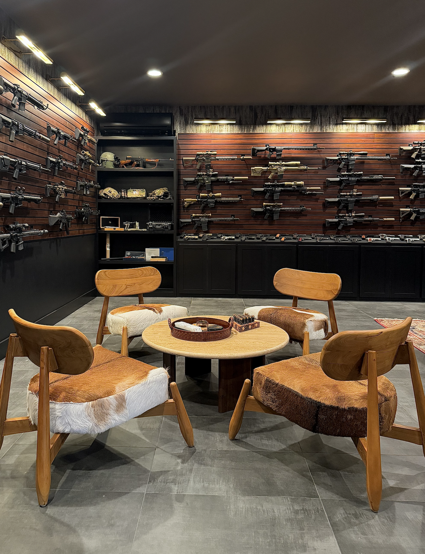 A room with a display of firearms mounted on dark wood-paneled walls and a table with four wooden chairs with animal print cushions.