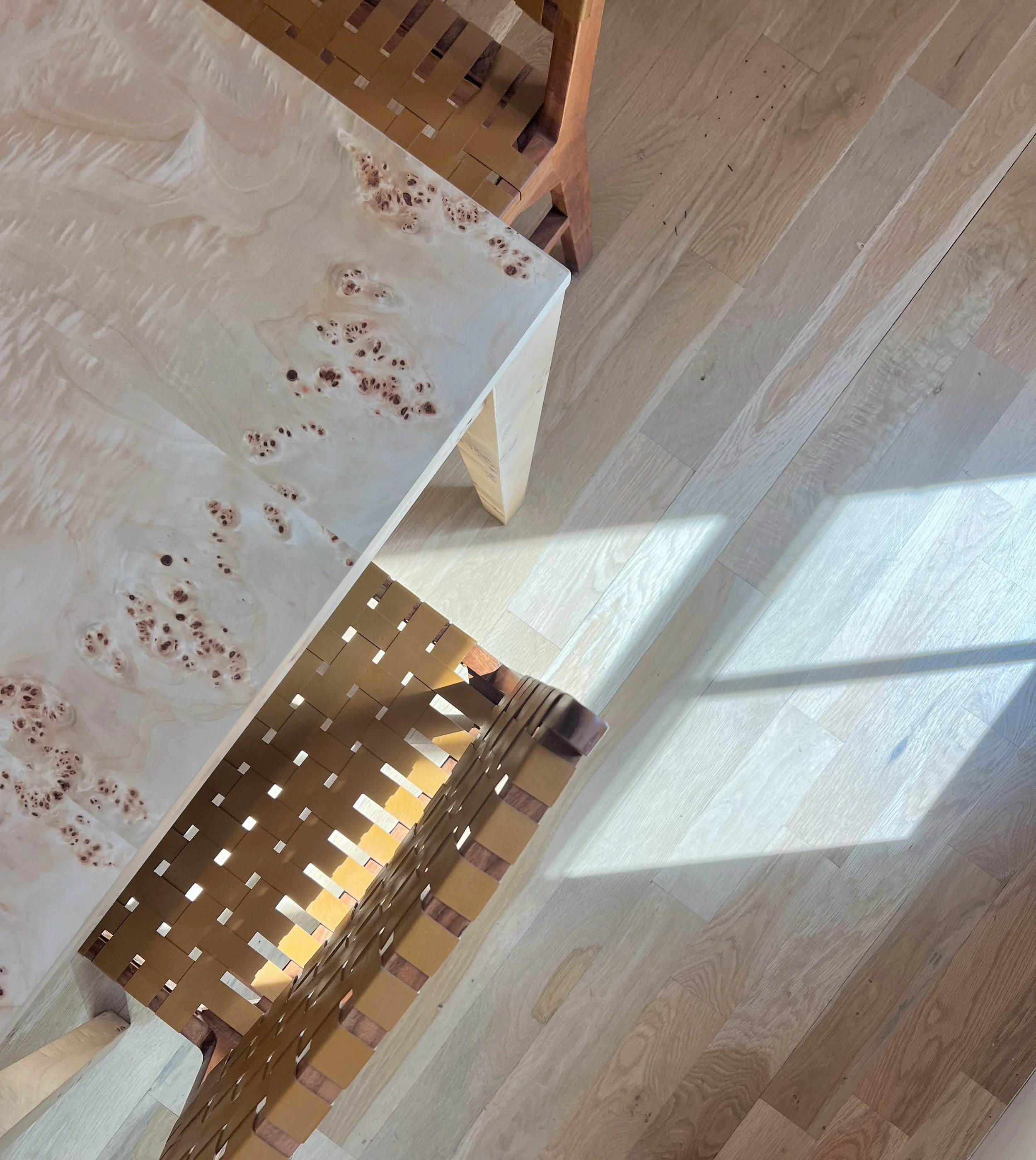 Top-down view of a marble dining table with a wood chair and a wicker chair on a light wooden floor with sunlight casting shadows.