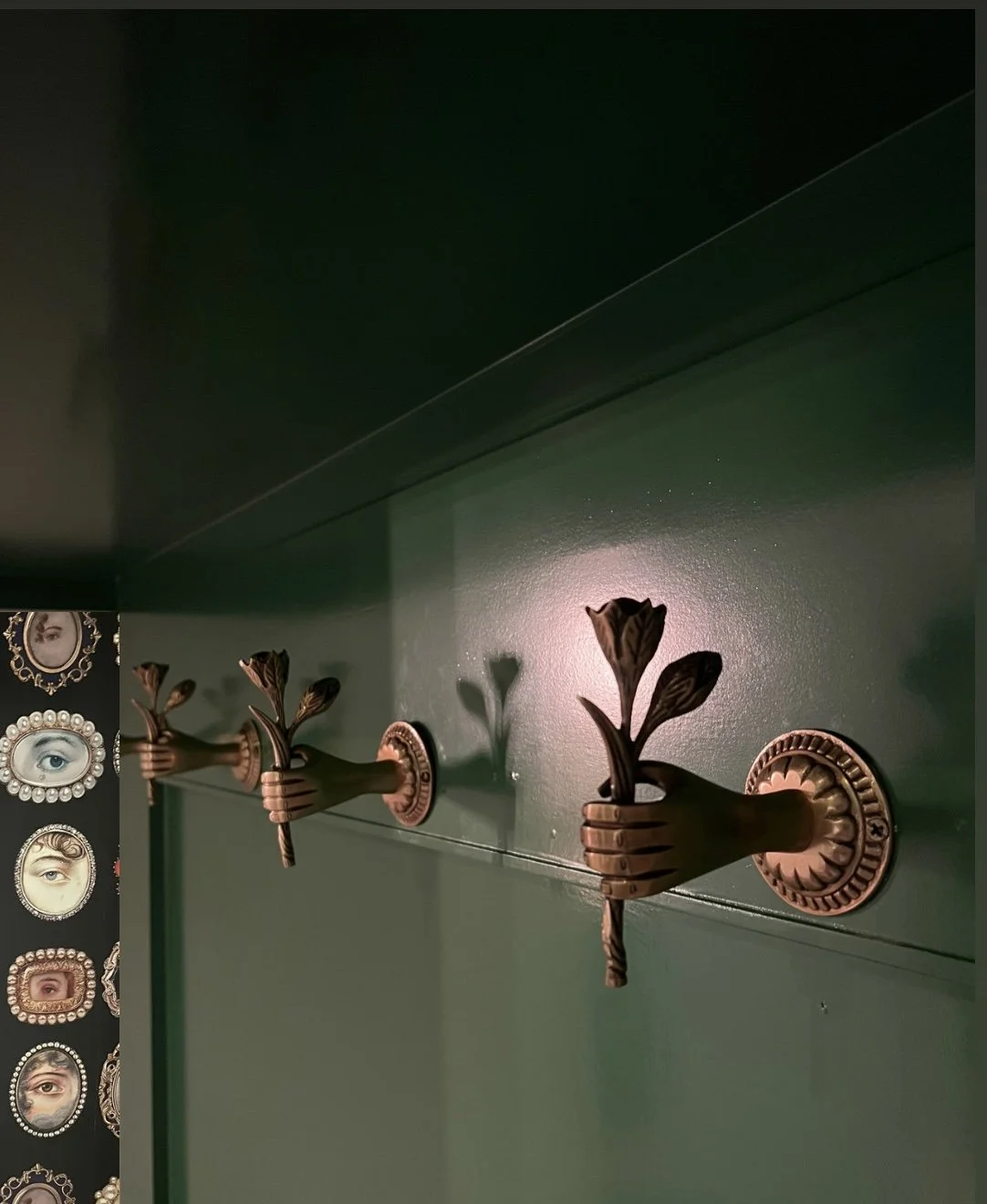 Three decorative wall hooks shaped like hands holding flowers, mounted on a green wall.