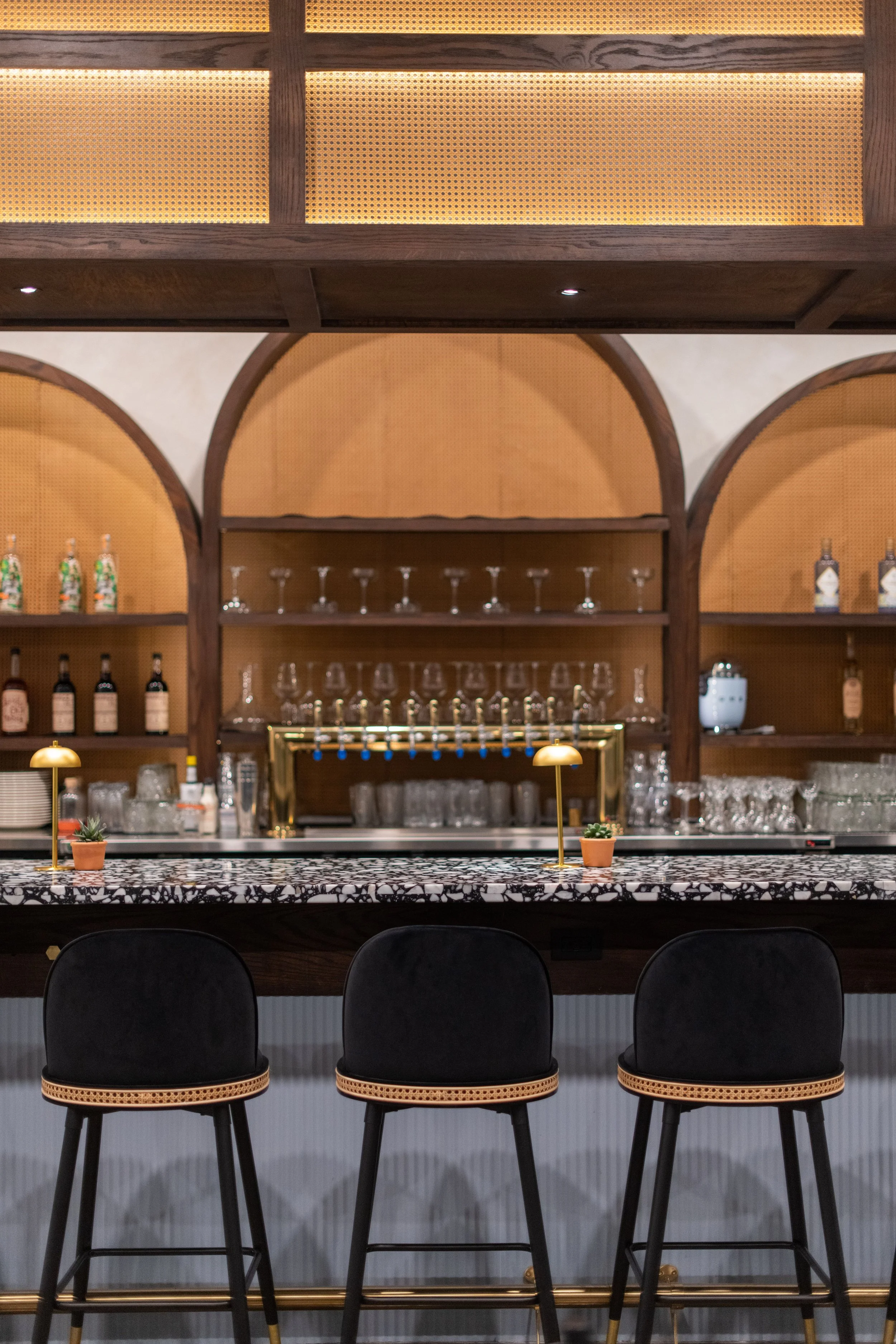 Modern bar interior with black barstools, a marble countertop, and shelves with glasses and bottles of alcohol