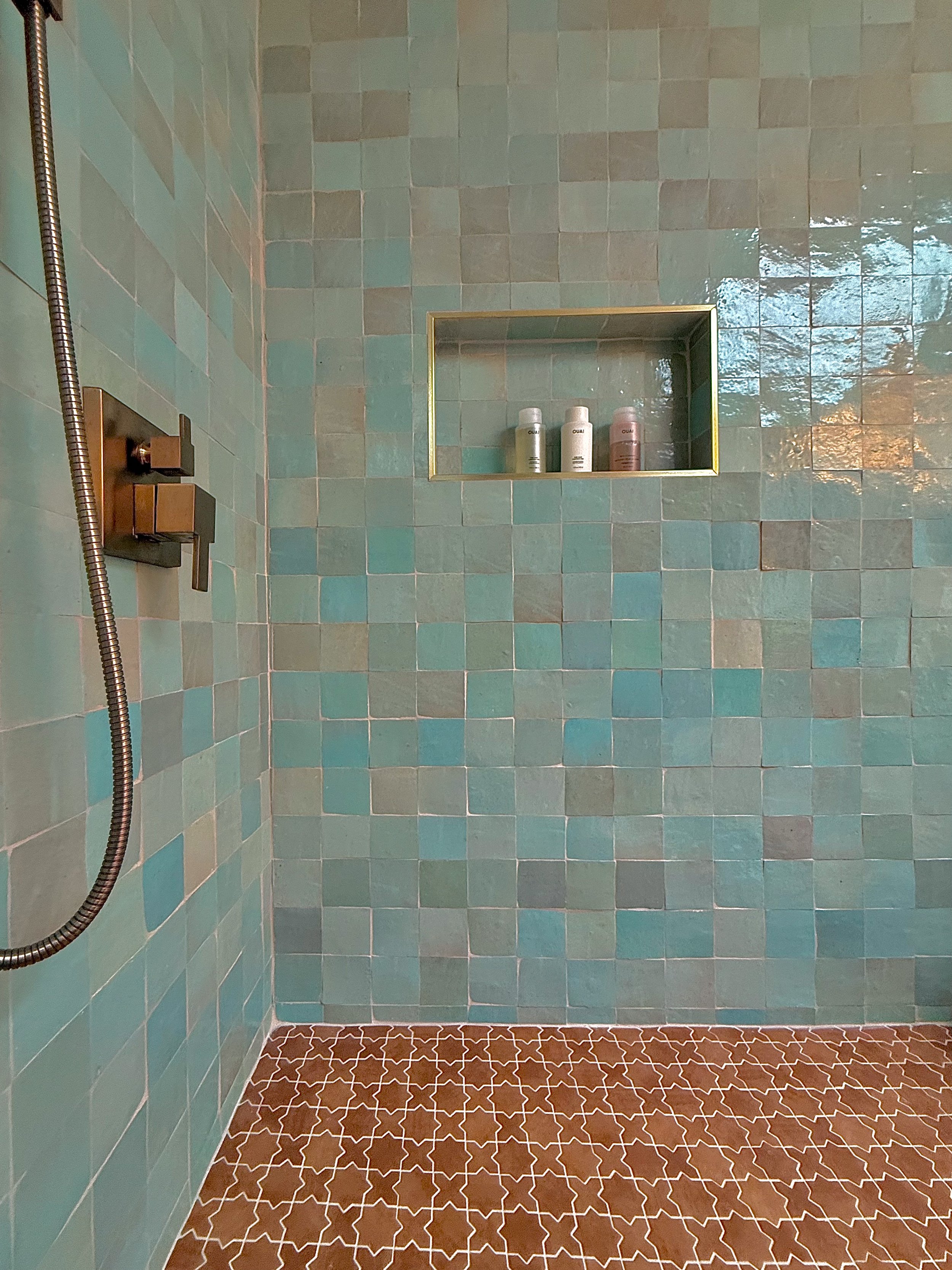 Shower with teal tiled wall, recessed shelf, and brown patterned tiled floor.