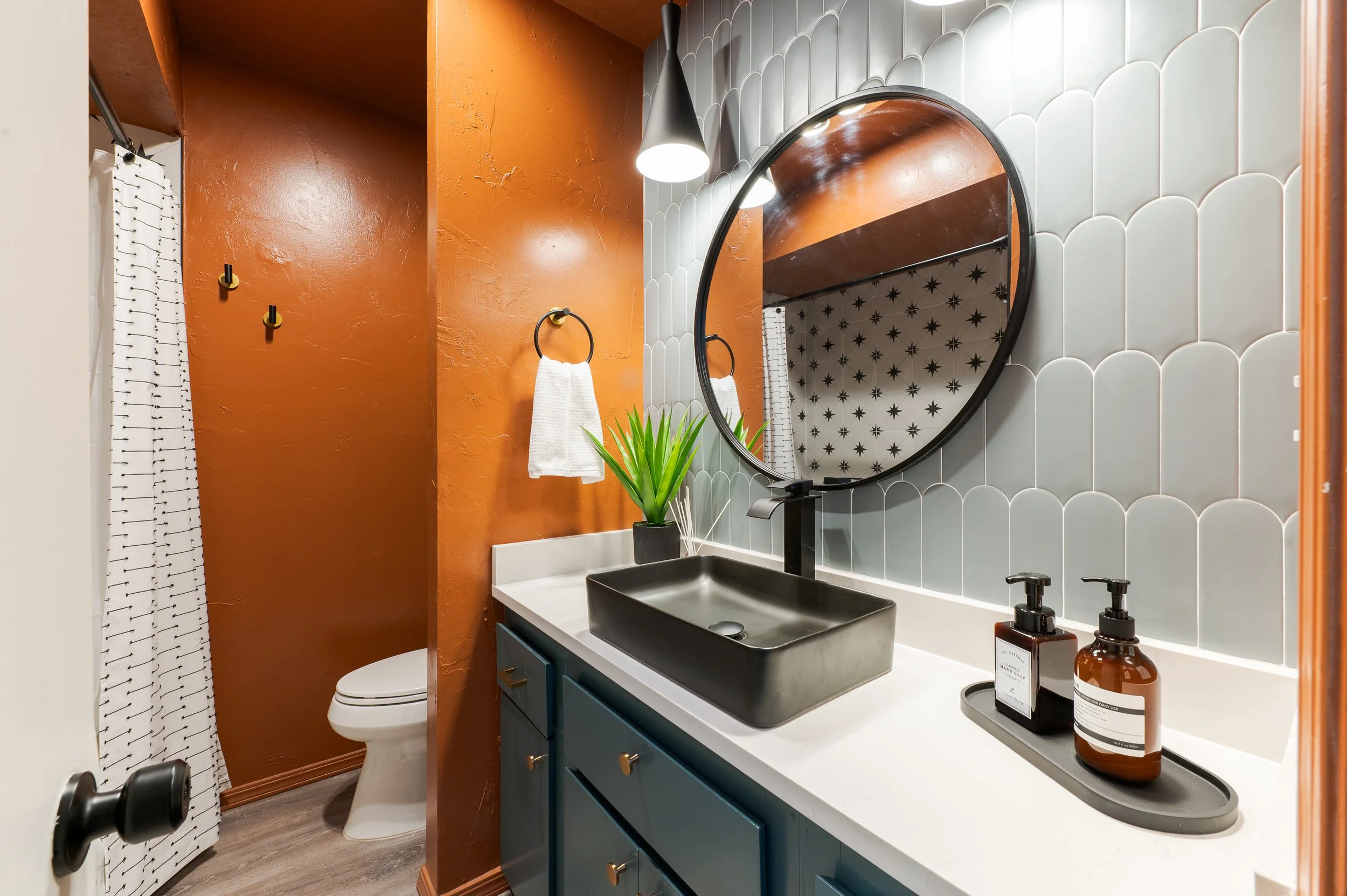 Modern bathroom with blue cabinet, black vessel sink, round mirror, star-patterned shower curtain, and terracotta-colored walls.