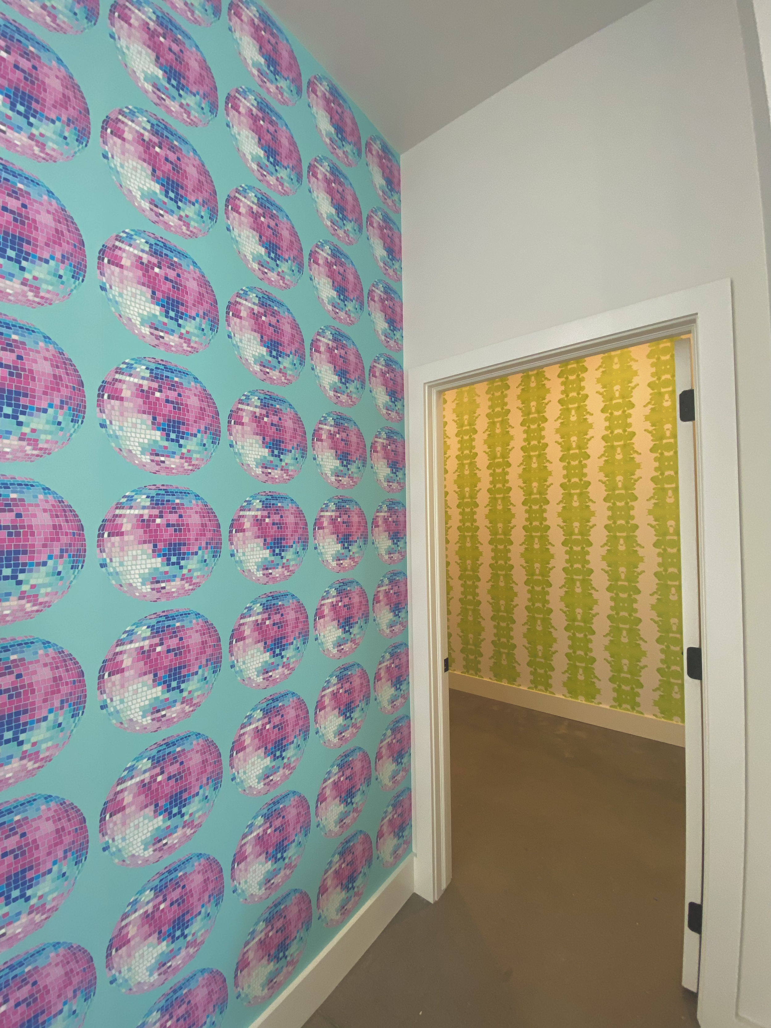 Interior hallway with colorful wallpaper featuring pink and purple disco balls on the left wall and yellow and green abstract patterned wallpaper on the back wall.