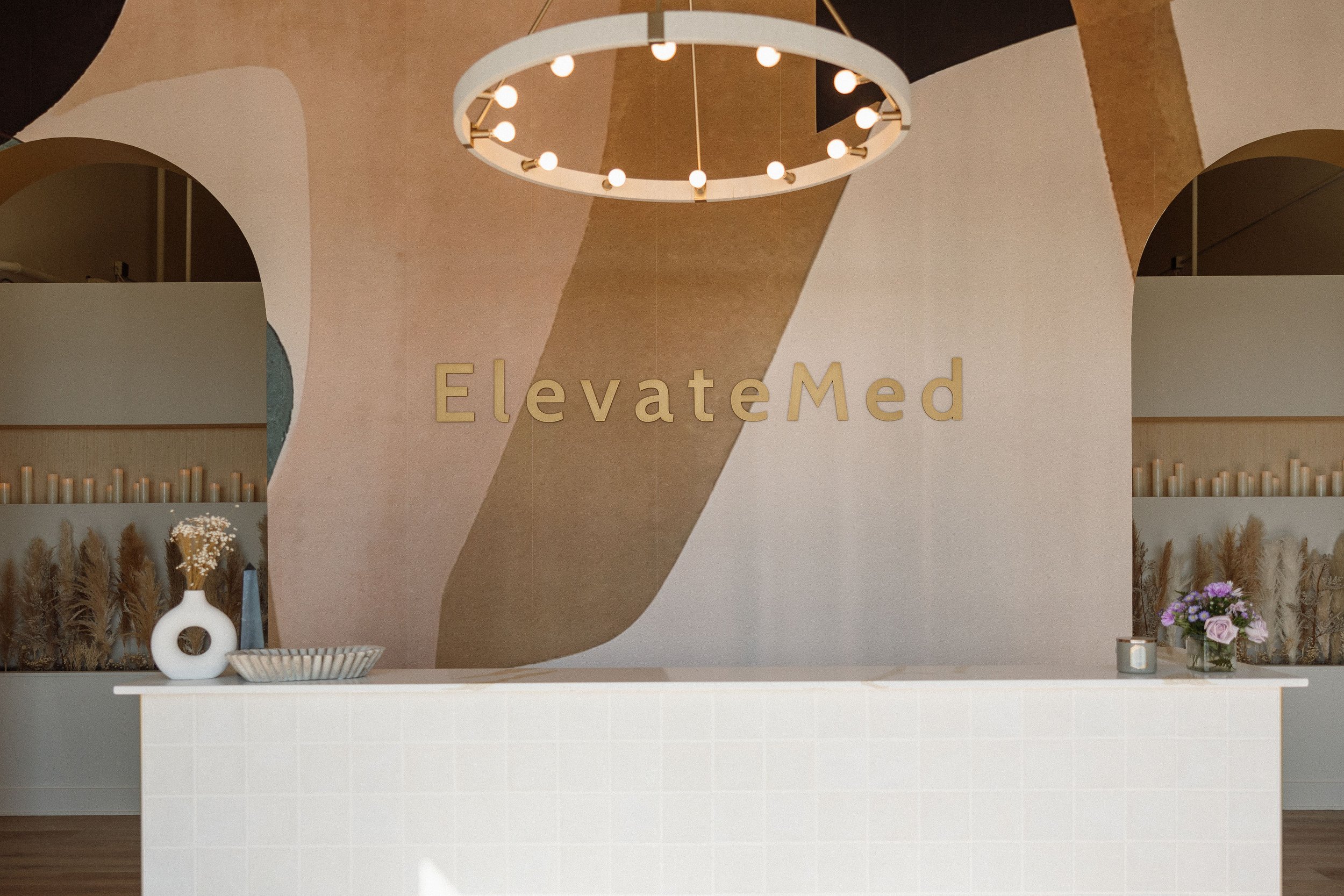 Modern reception desk with the sign 'ElevateMed' behind it, decorated with vases of flowers and candles in a neutral-toned interior with soft lighting.