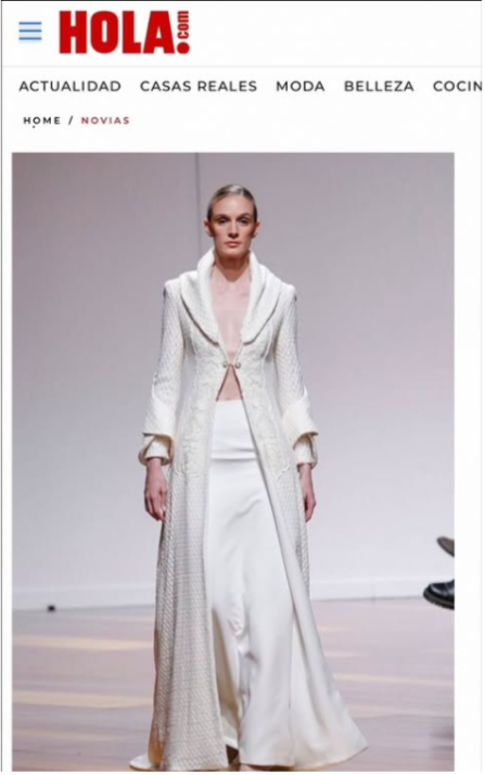 Modelo caminando en pasarela con vestido largo y abrigo blanco en desfile de moda