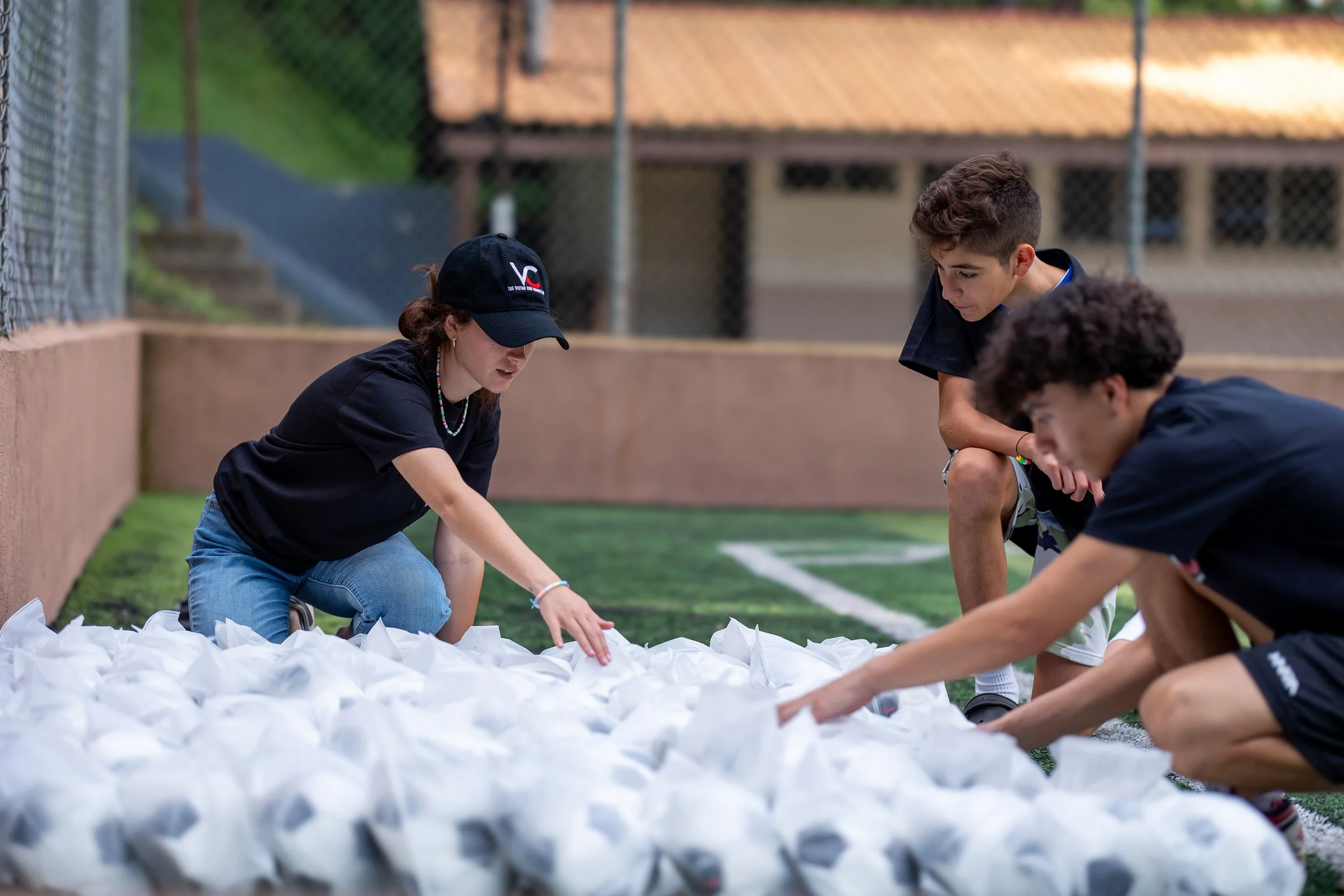 Tres jóvenes colocando bolsas de papel en un campo de césped, posiblemente como parte de una actividad de limpieza o voluntariado.
