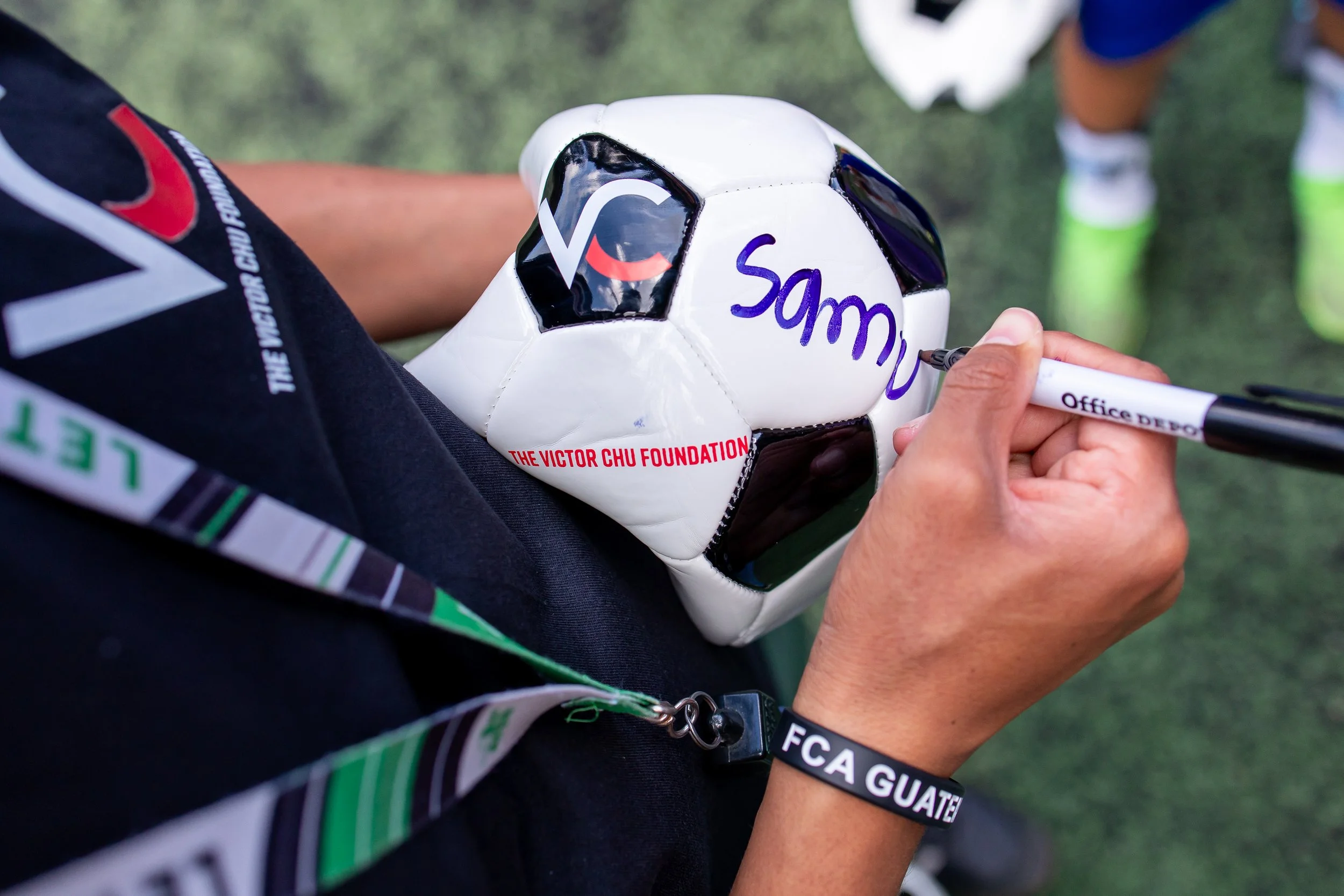 Persona autografiando un balón de fútbol con la palabra 'Sammy' en un campo de césped.