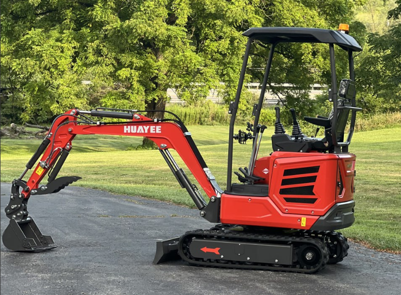 A red mini excavator with the brand name 'HUAYEE' on the arm, parked on a paved surface with grass and trees in the background.