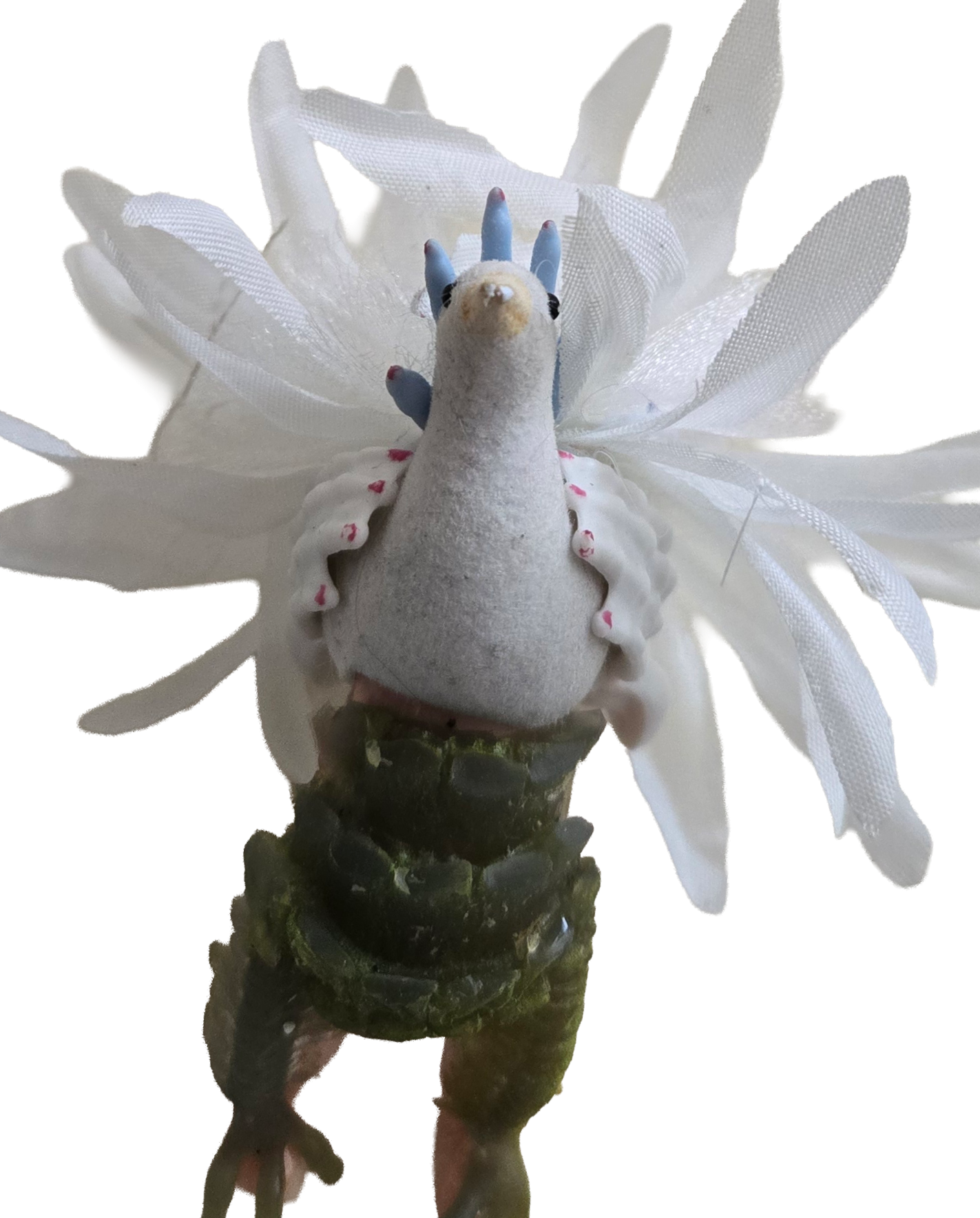 A mashed up monster made of toys. It has green feet, the body and head of a goose, blue monster hands on its sides and a white tail made of petals.