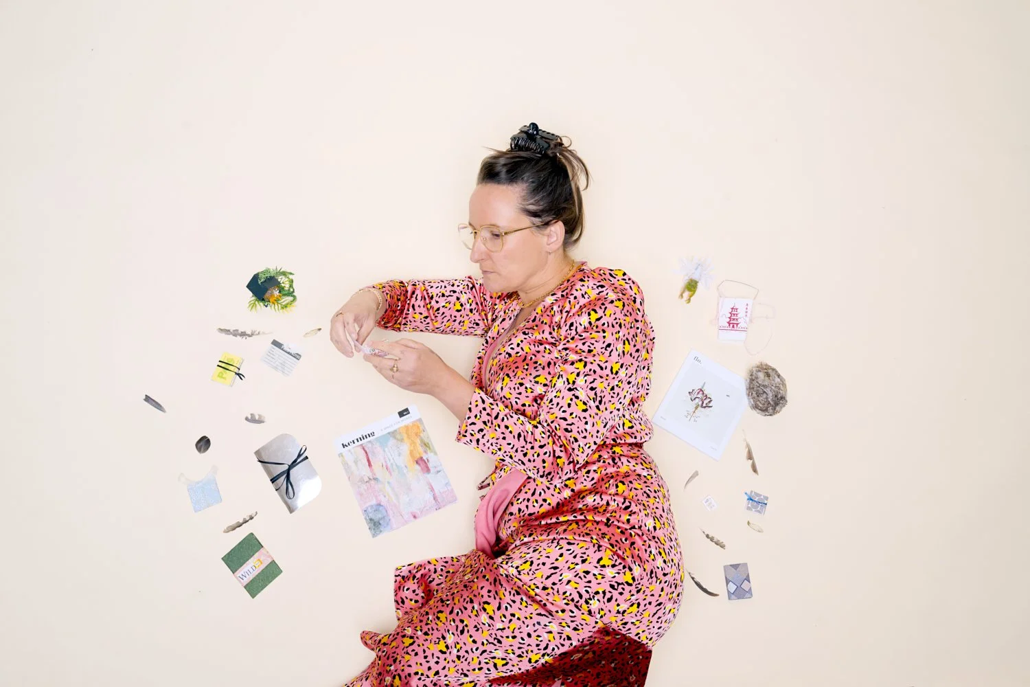 Woman in pink leopard print pajamas lying on beige background amid scattered small objects and papers.