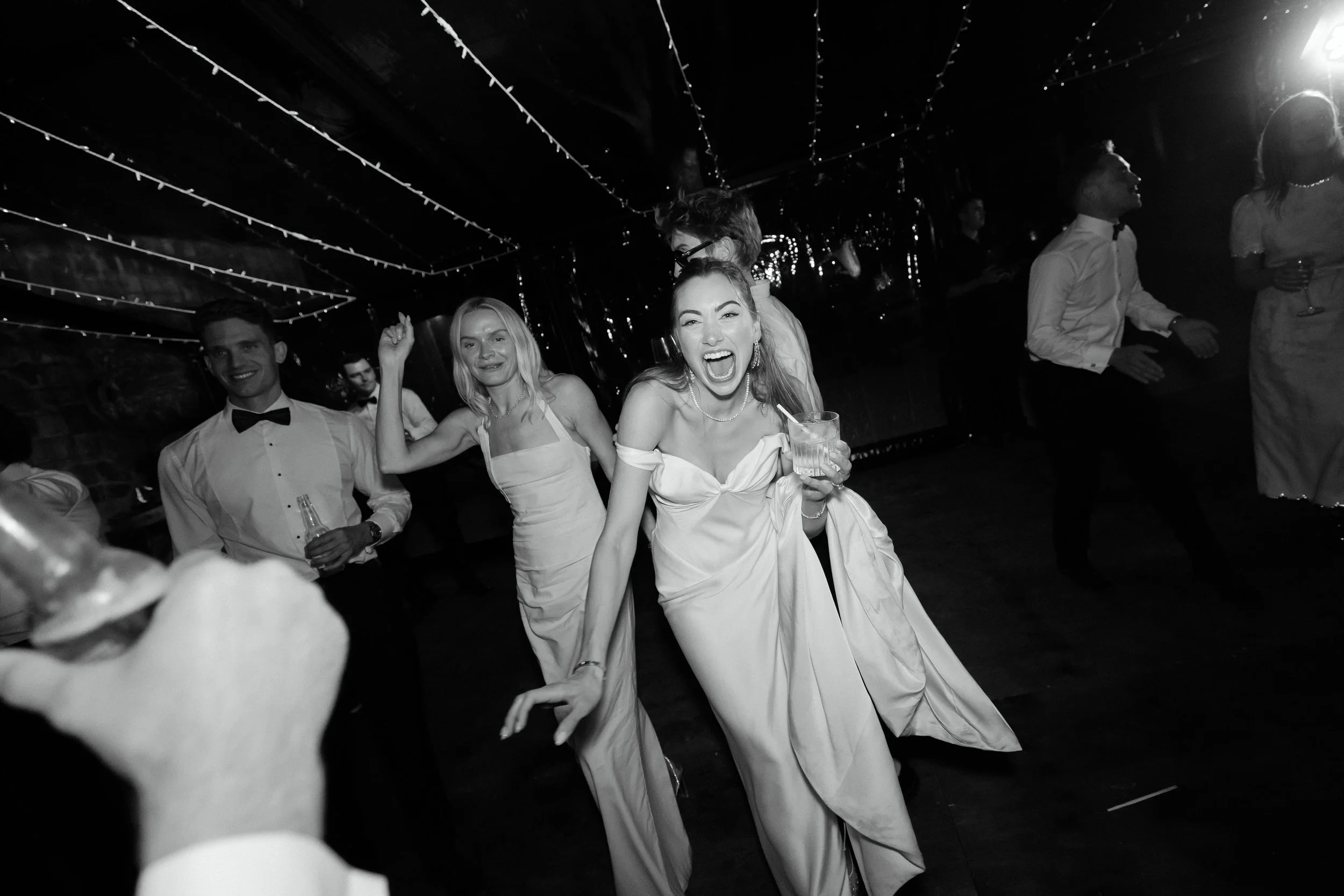 People dancing and celebrating at a party, with festive lighting overhead.