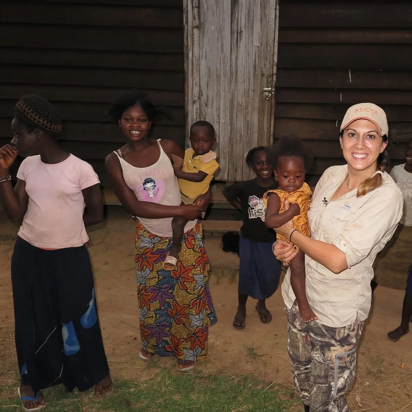 A woman holding a young girl in a yellow dress, surrounded by smiling children in rural Africa, Congo