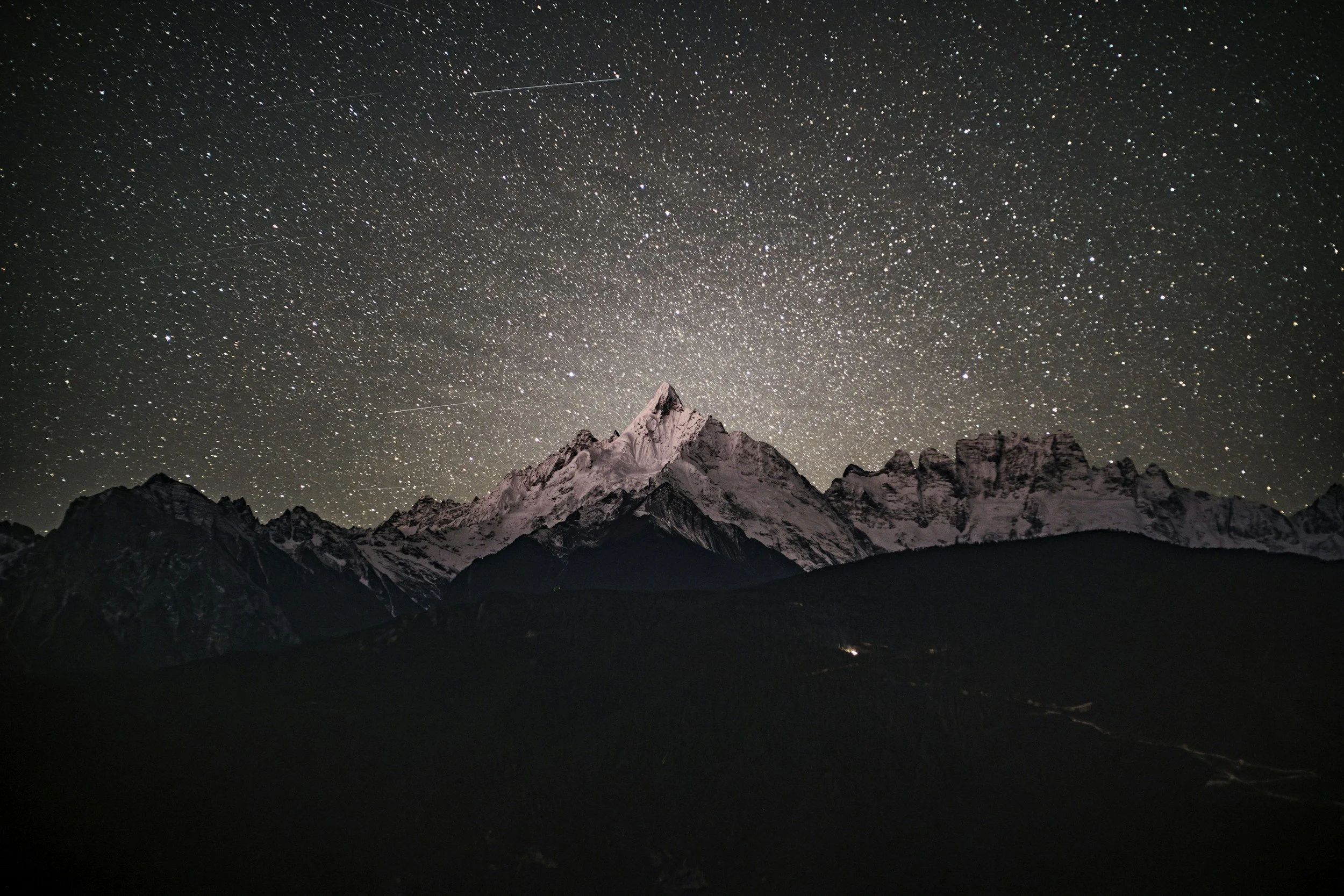 Night sky filled with stars over snow-capped mountain peaks.