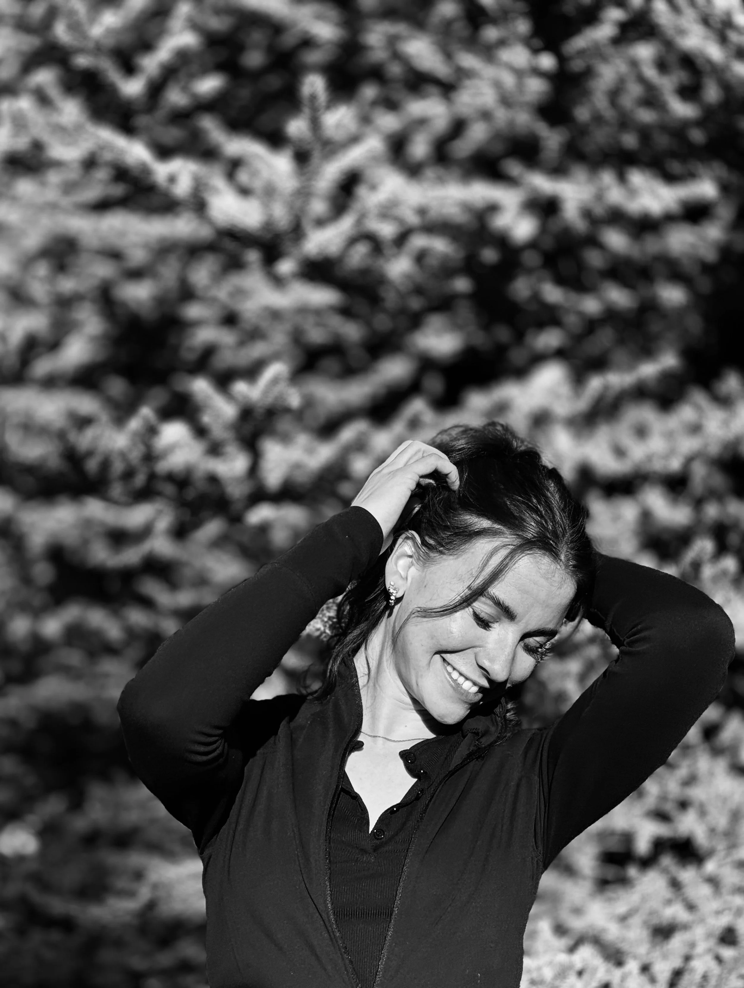 Smiling woman with closed eyes, holding her hair back with both hands, outdoors on a sunny day.