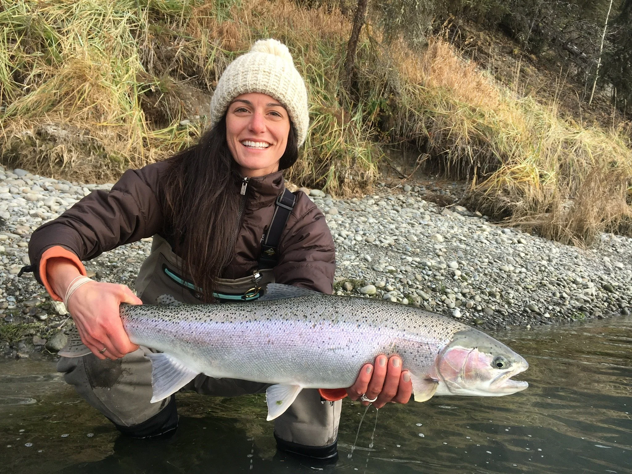 A woman smiling and holding a large fish while standing in a river.