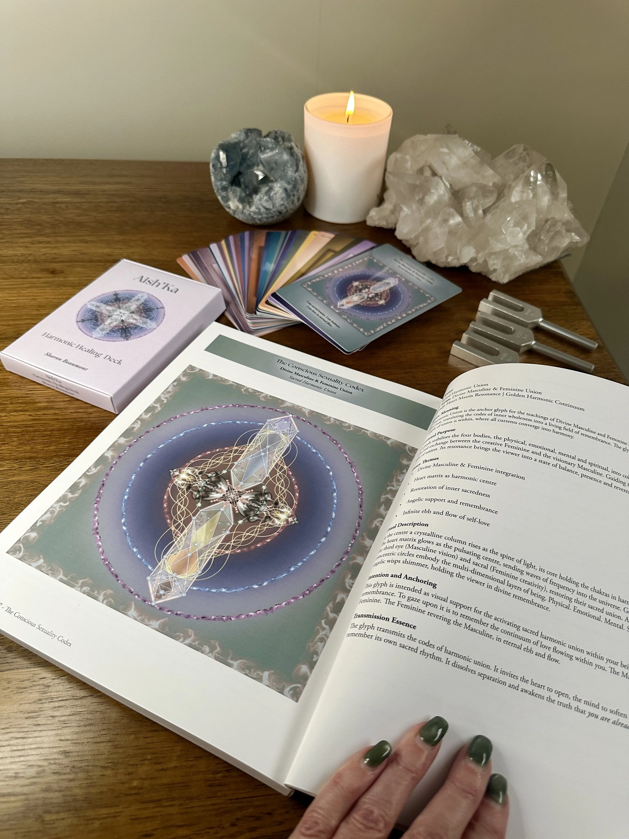 Aish'Ka Harmonic Healing Codex and card deck displayed with crystals, candle and tuning forks in a peaceful ritual space.