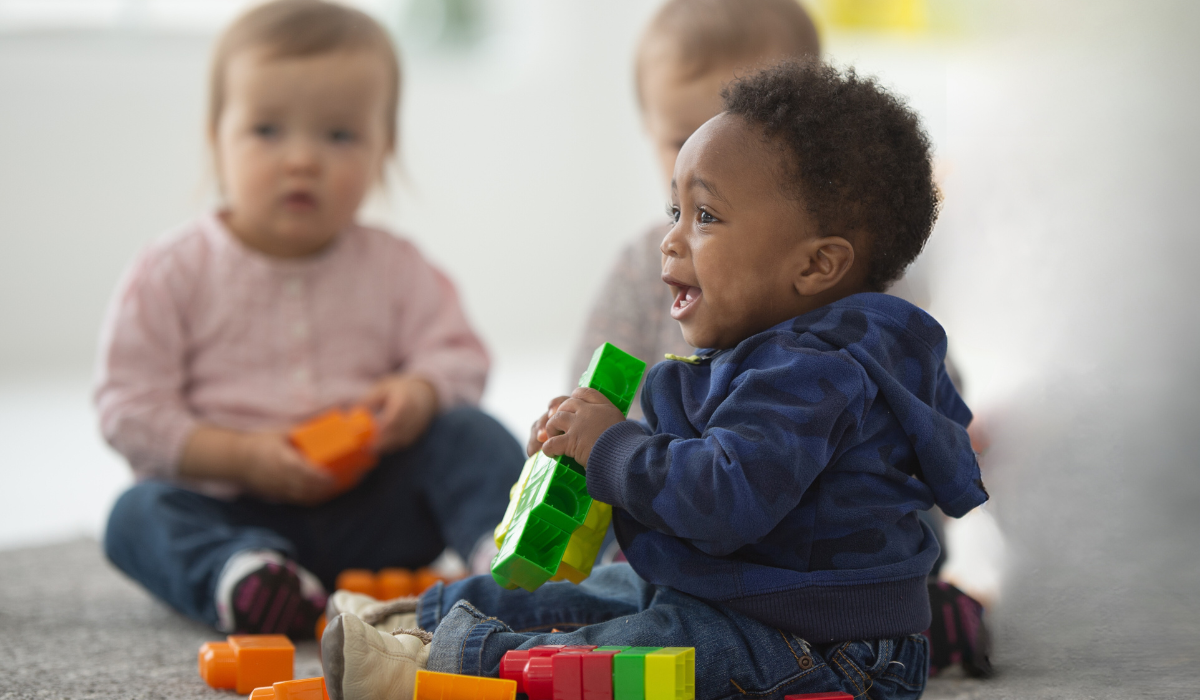 Three young children sitting on the floor playing with colorful building blocks.