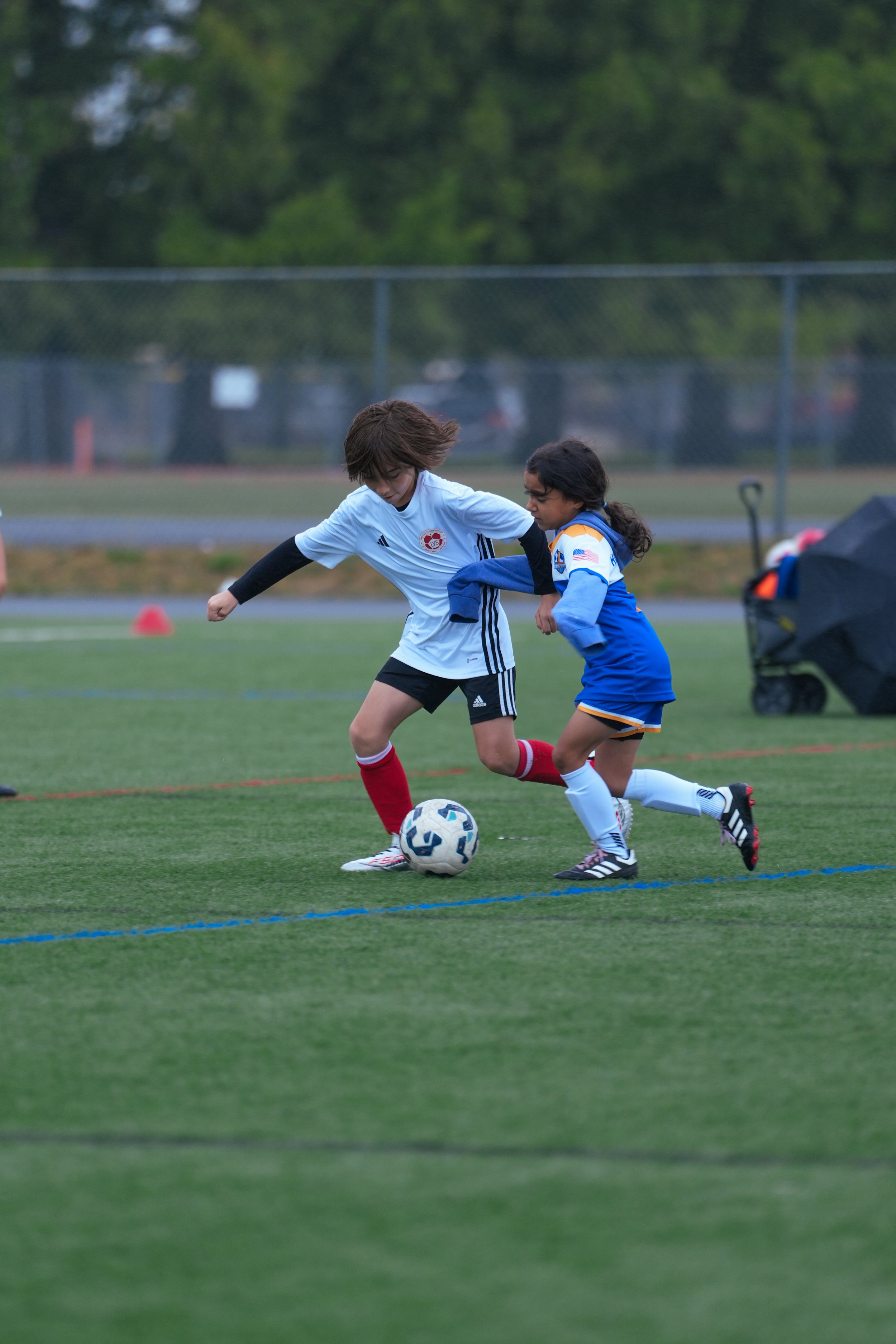 Two young girls playing soccer on a field, fighting for control of the ball.