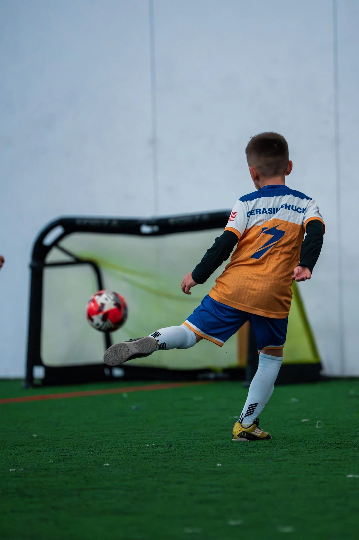 Young boy playing indoor soccer, kicking a ball towards a goal.