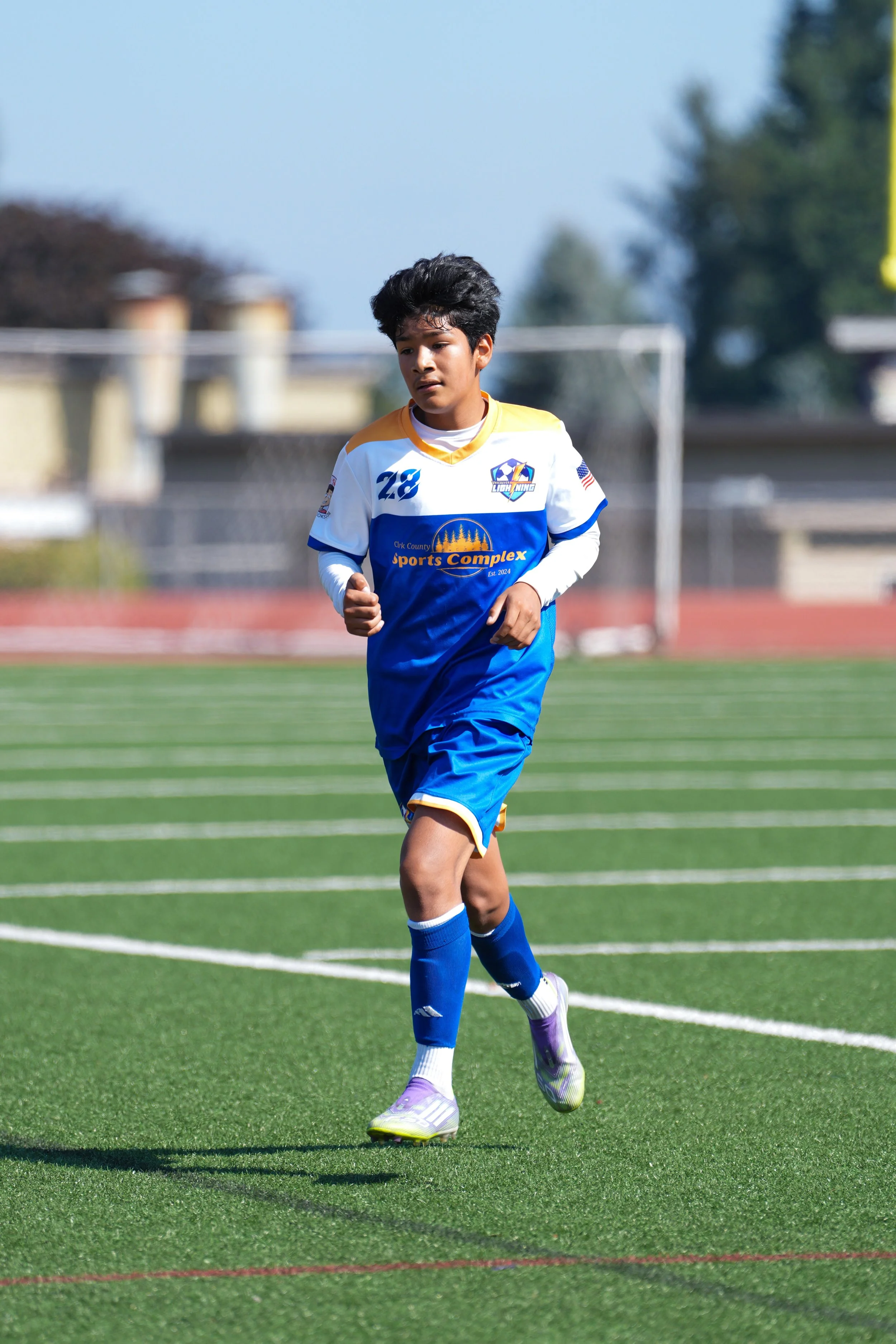 A young male soccer player in a blue and white uniform running on a soccer field.