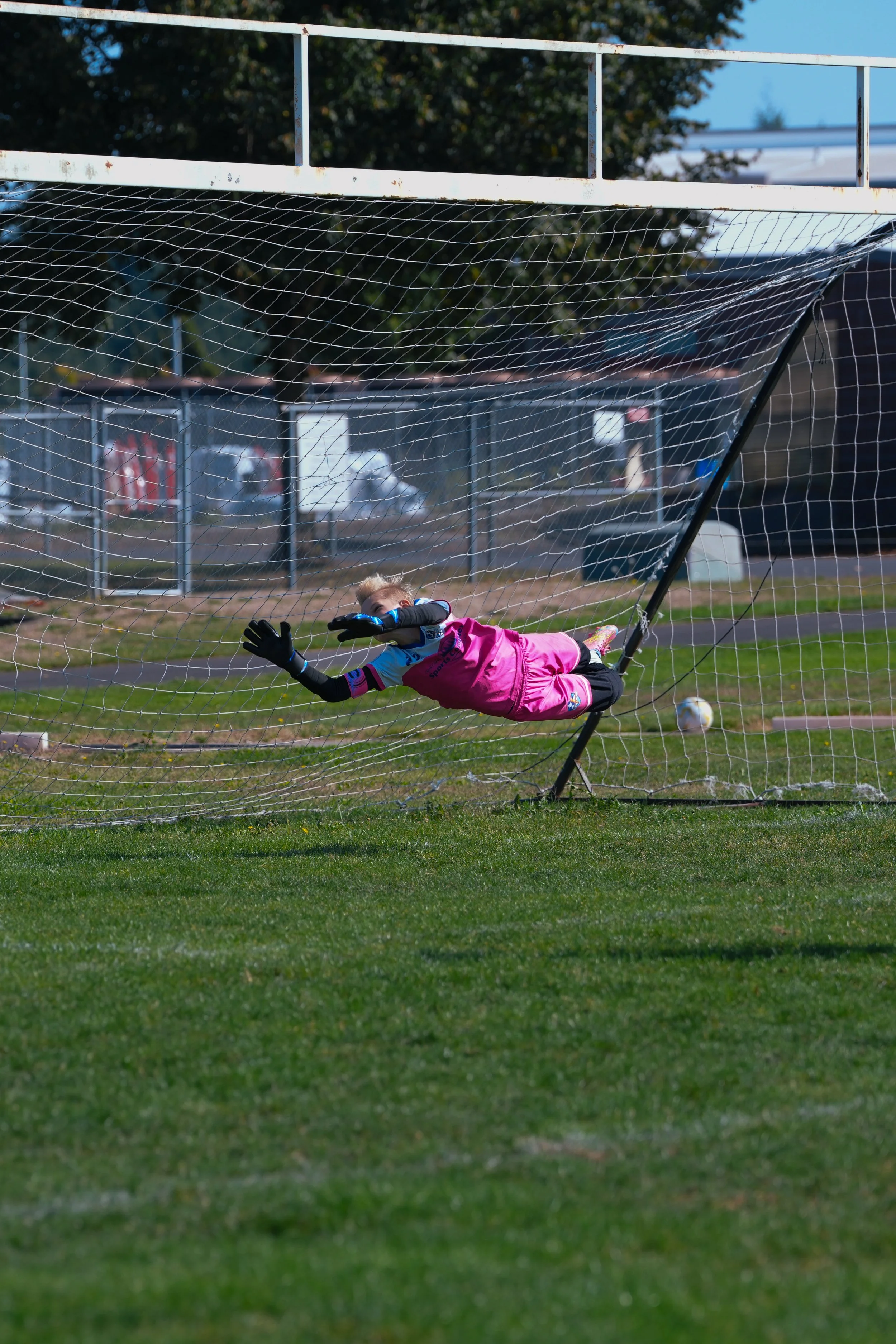 A young soccer goalkeeper diving to save a shot on goal during a game.