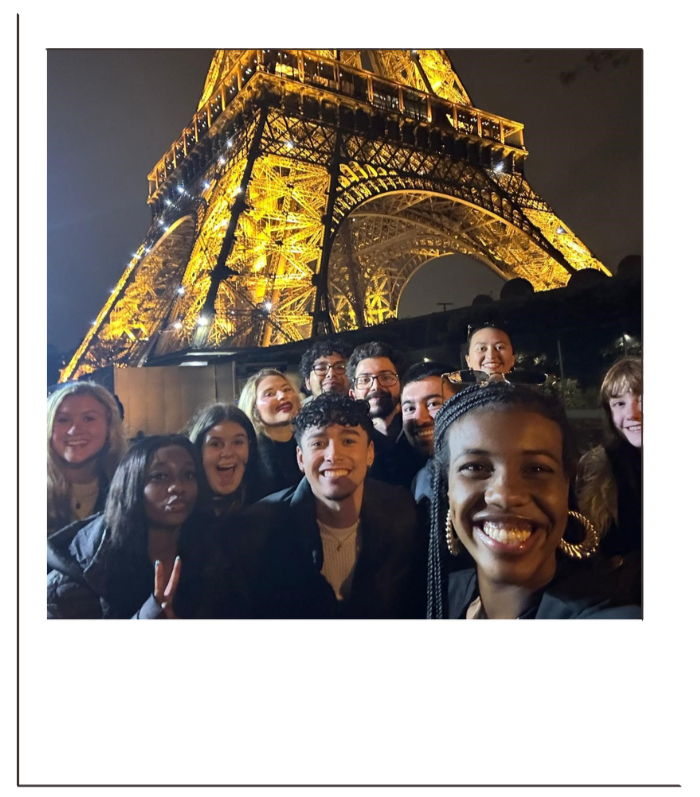 A group of people taking a selfie in front of the illuminated Eiffel Tower at night.