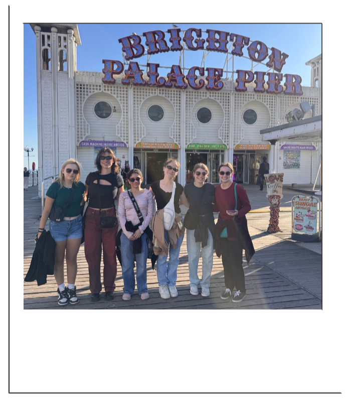 Group of six women standing in front of Brighton Palace Pier entrance on a sunny day.
