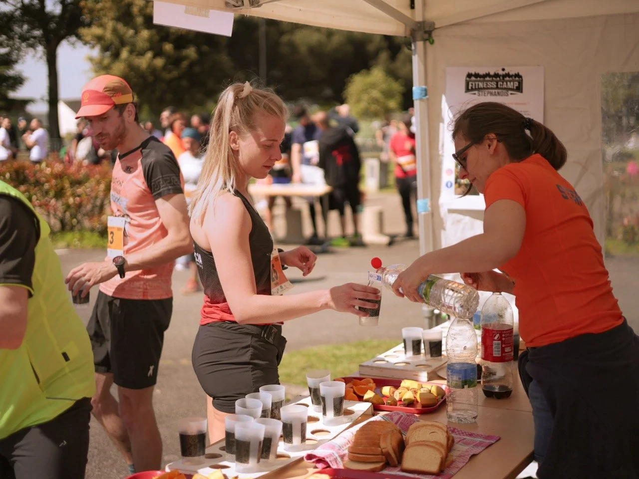 Des bénévoles distribuent de l'eau et des snacks à des coureurs lors d'une course en plein air.