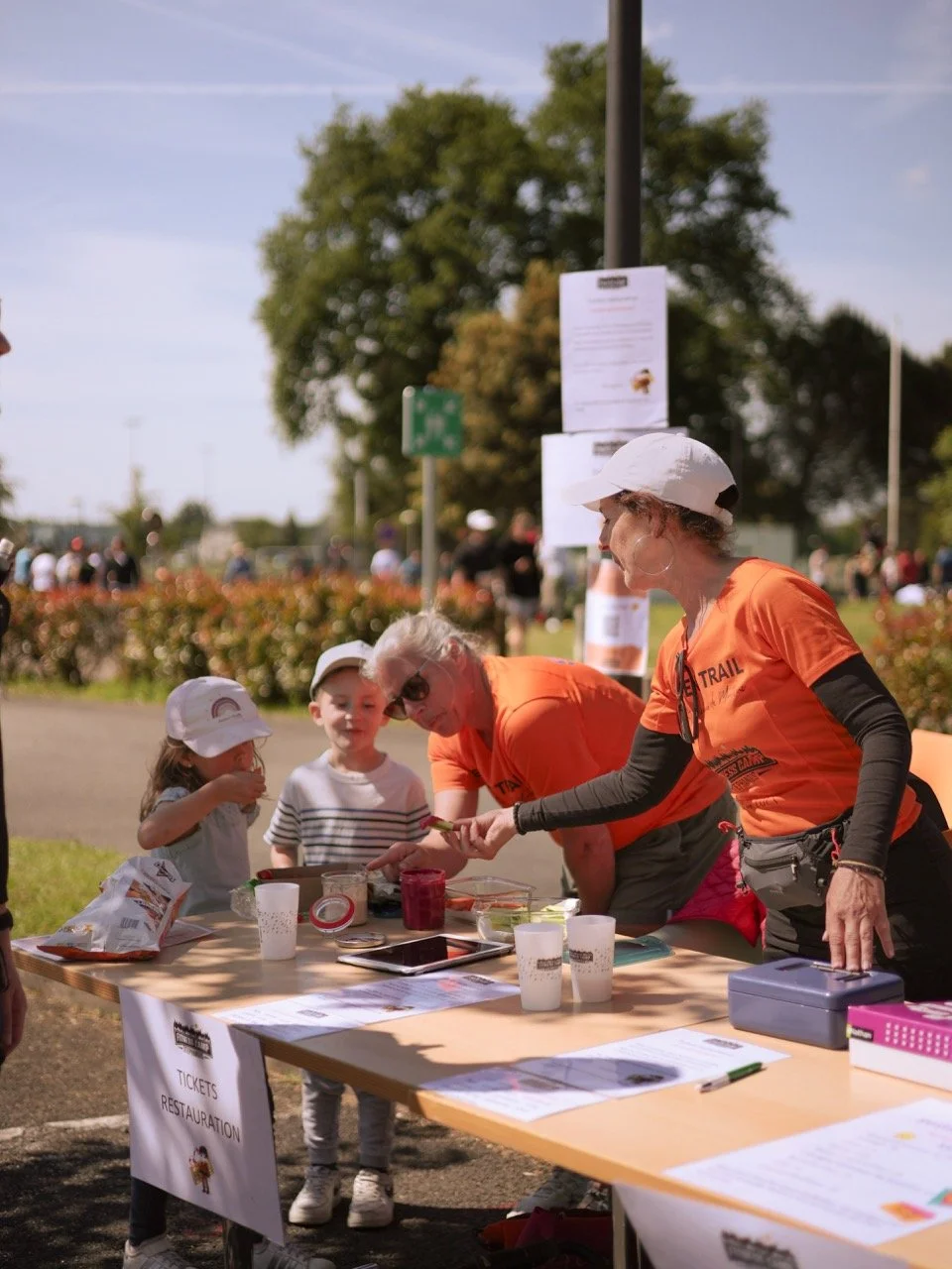 Des bénévoles en t-shirts orange aidant à une table d'information lors d'un événement en plein air