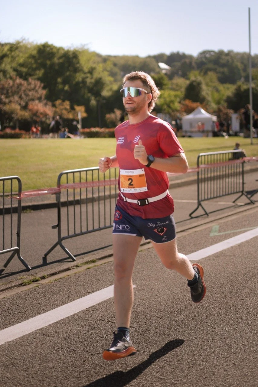 Un homme court lors d'une course en plein air par une journée ensoleillée, portant une tenue de course rouge, des lunettes de soleil et une montre.»