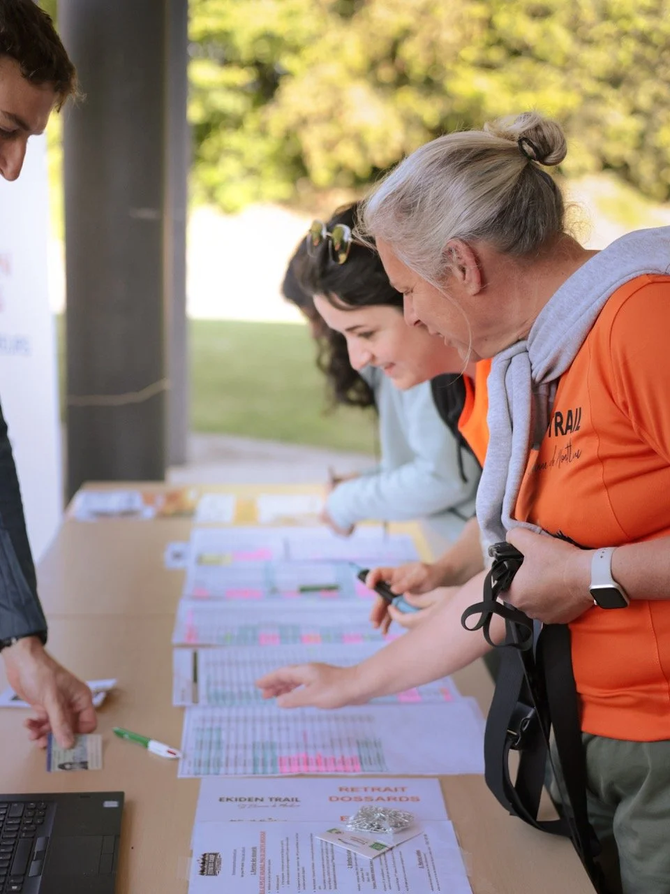 Groupe de personnes vérifiant des documents sur une table lors d'un événement en plein air, la journée.