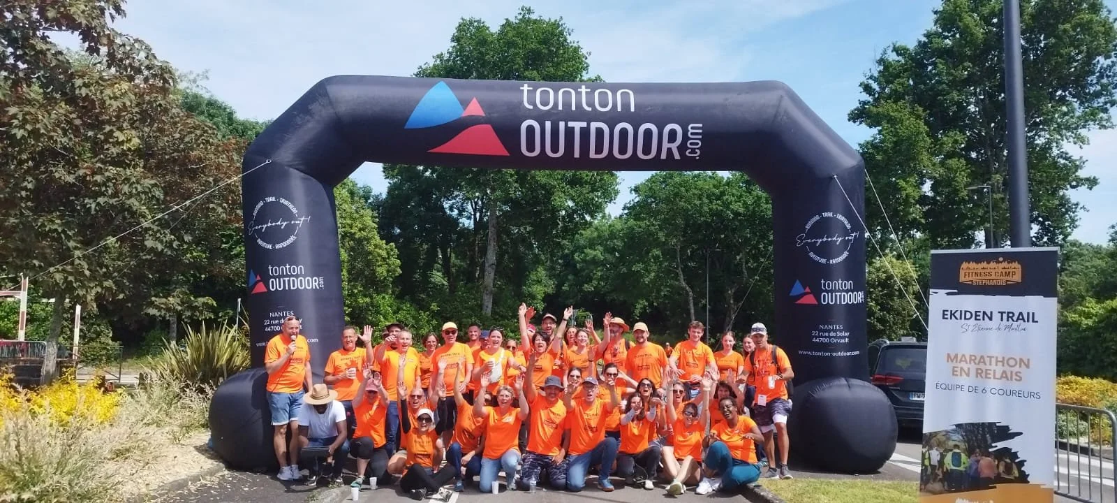 Groupe de coureurs en orange posant sous une arche gonflable avec le logo tonton OUTDOOR, devant un panneau indiquant un marathon relay.