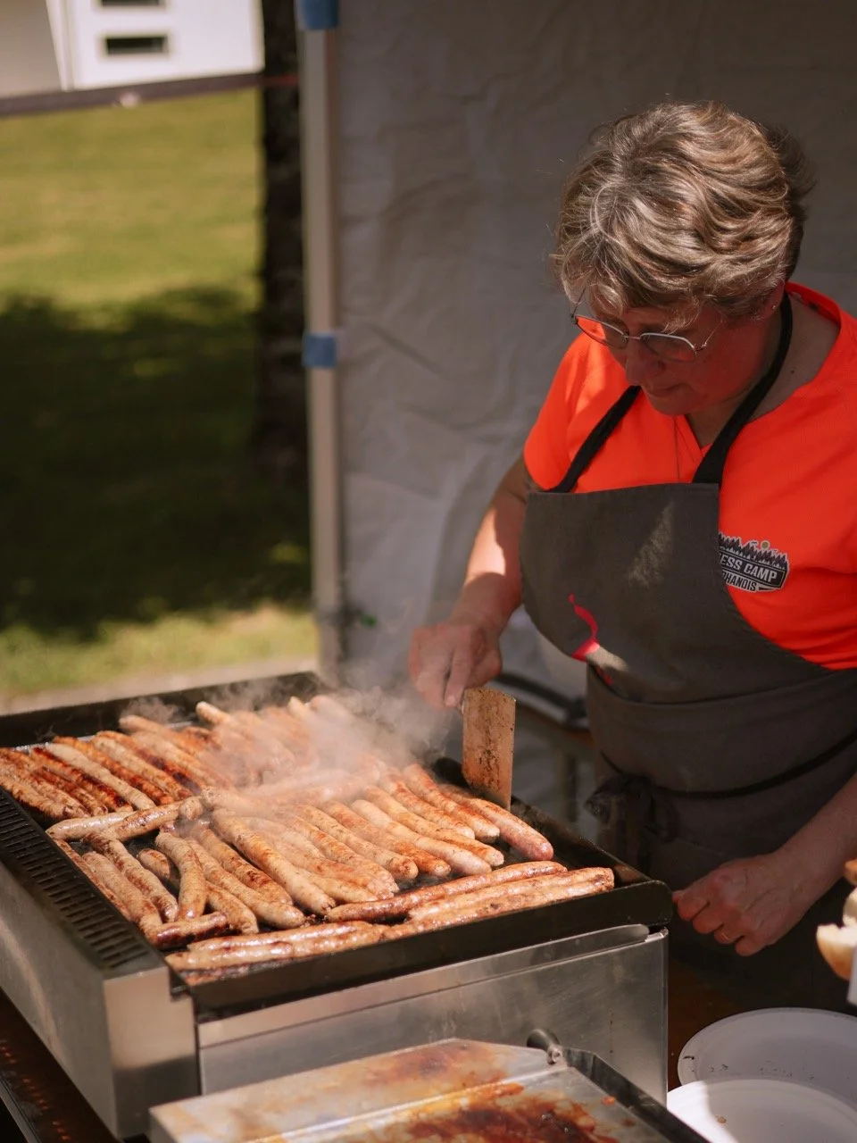 Une personne grille des saucisses sur un barbecue lors d'un événement en plein air.