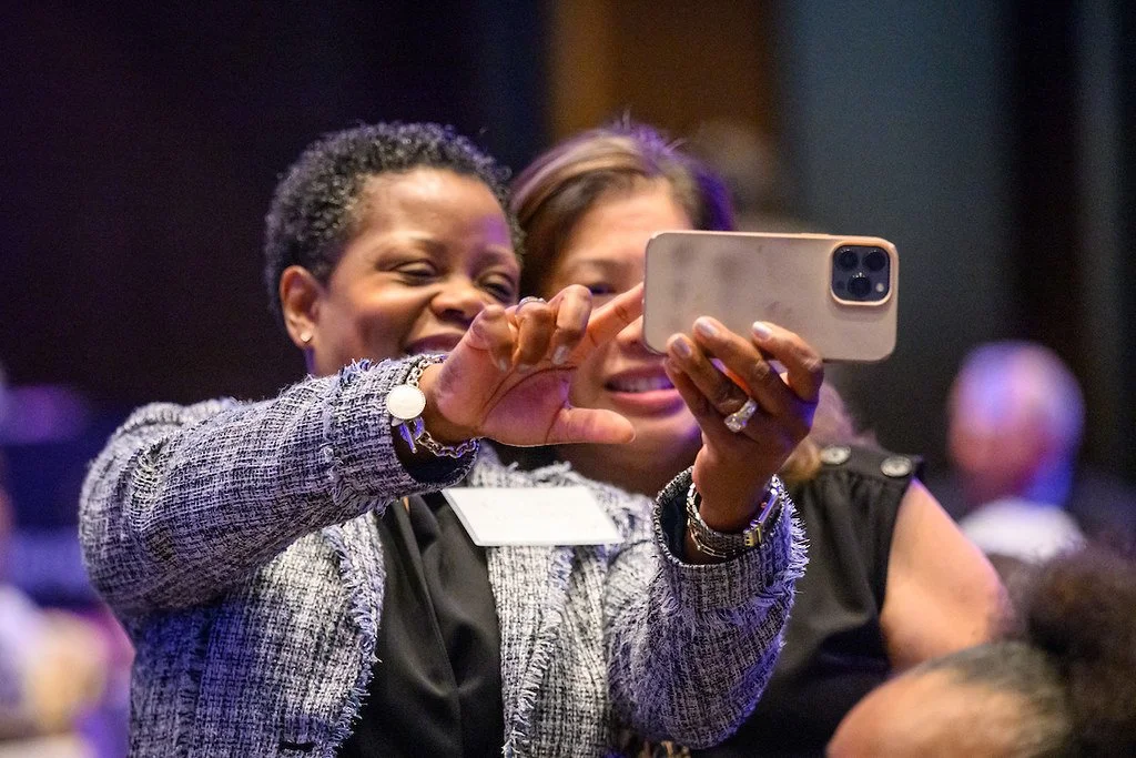 Two women smiling and taking a selfie together at an event.