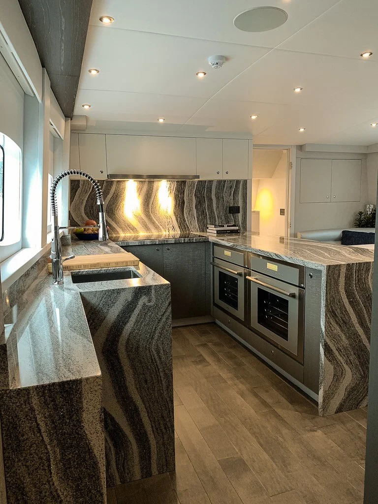 Modern kitchen with marble countertops and backsplash, stainless steel appliances, and wood flooring.