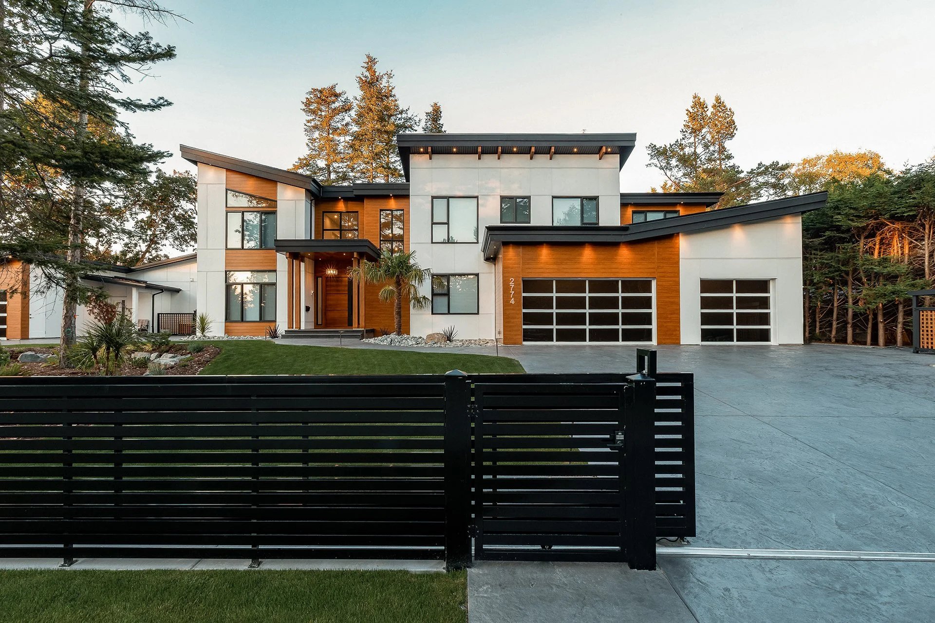 Modern two-story house with a combination of white and wooden exterior, large windows, and a black driveway gate in the foreground