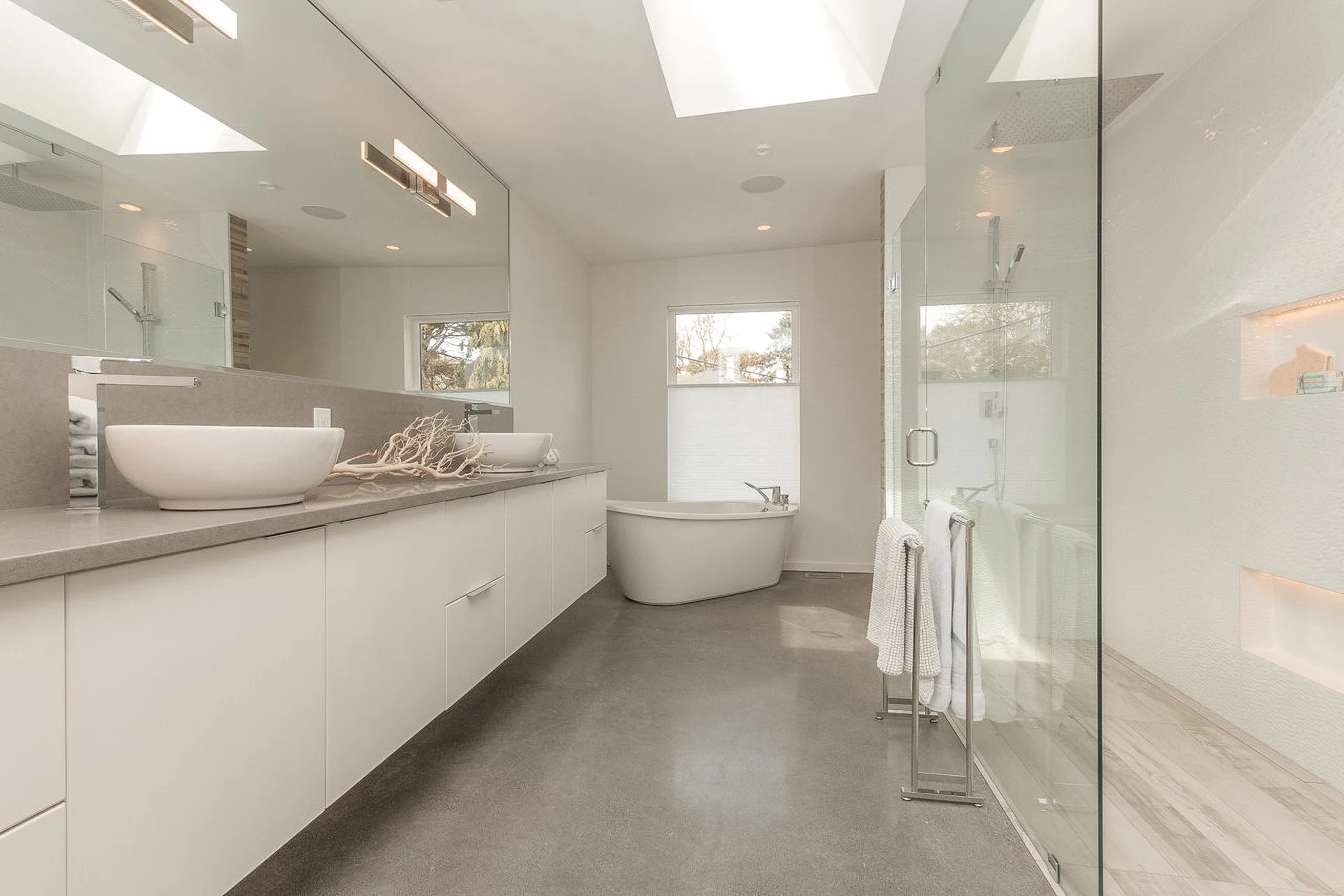 Modern bathroom with double sinks, bathtub, glass-enclosed shower, and large mirror.