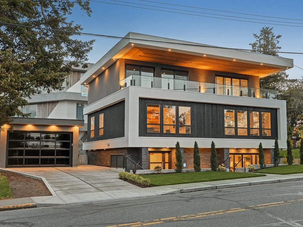 Modern multi-story house with large windows, a garage, and a landscaped yard at dusk.