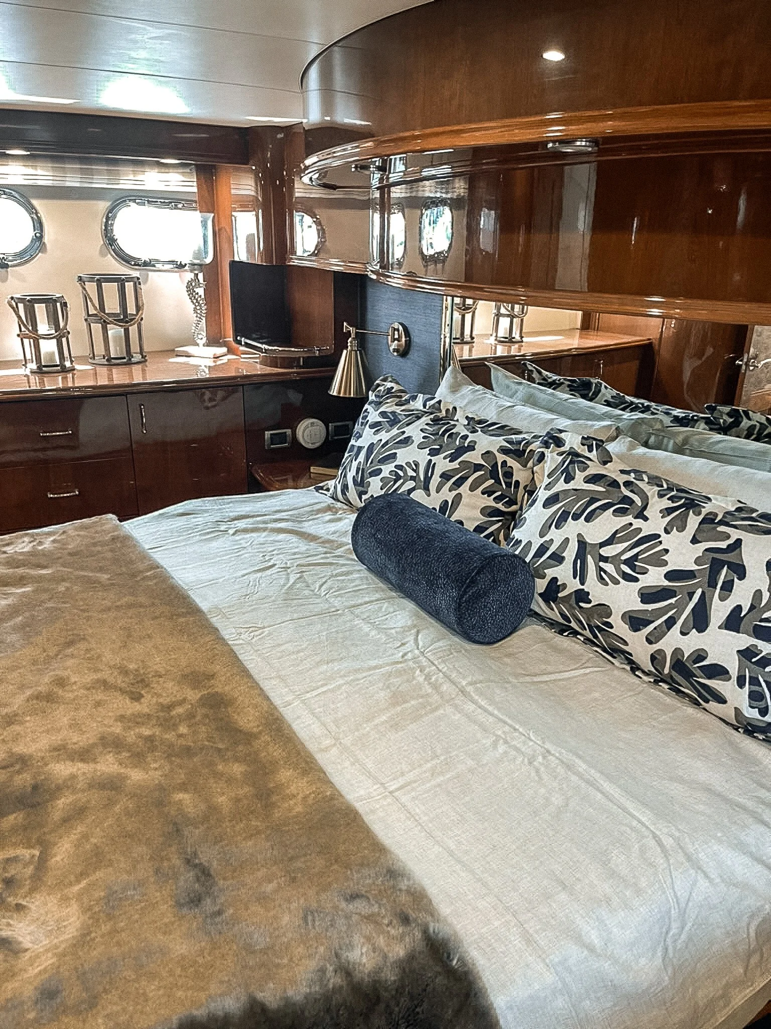 A luxurious bedroom with a large bed covered in white and patterned pillows, inside a wood-paneled room with porthole windows.
