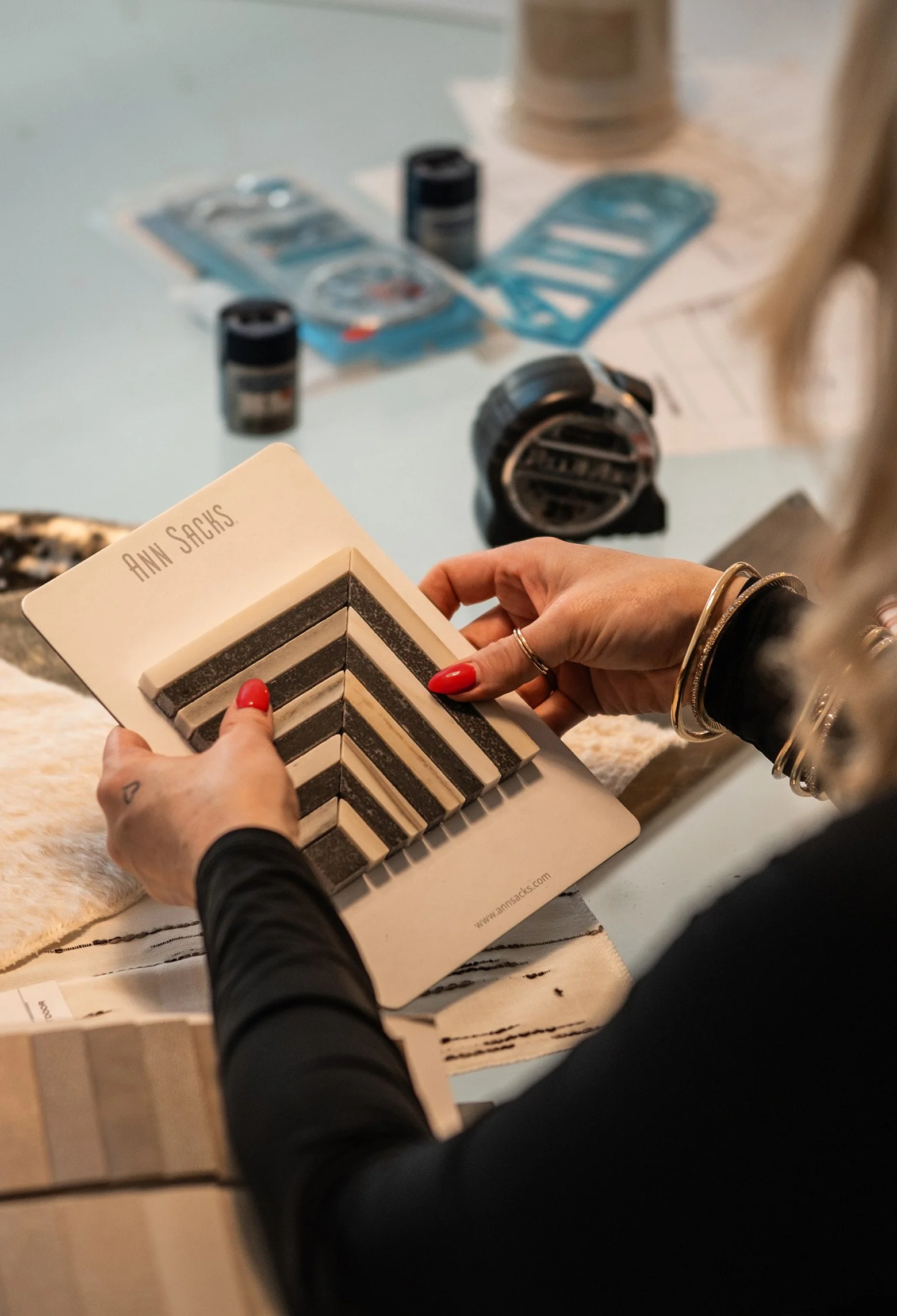 Person holding a sample swatch card from Ann Sacks for tile or design selection, looking at black, white, and beige tile options.